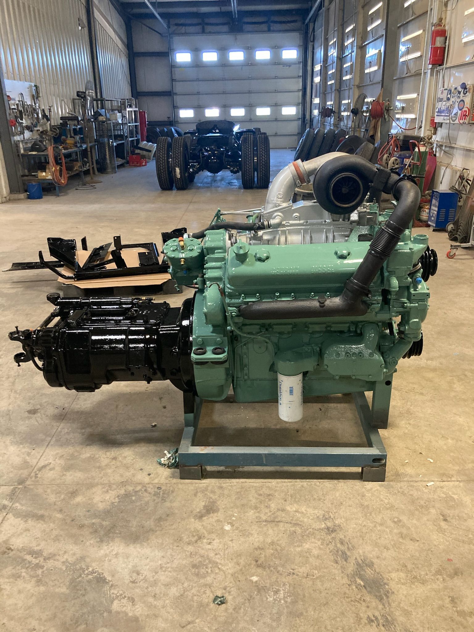 Green truck engine with black parts on a metal stand in a workshop.