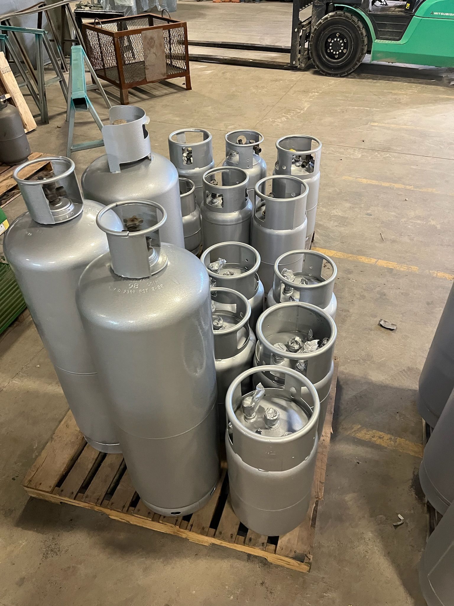 Silver propane tanks on a wooden pallet in a warehouse, with a forklift in the background.