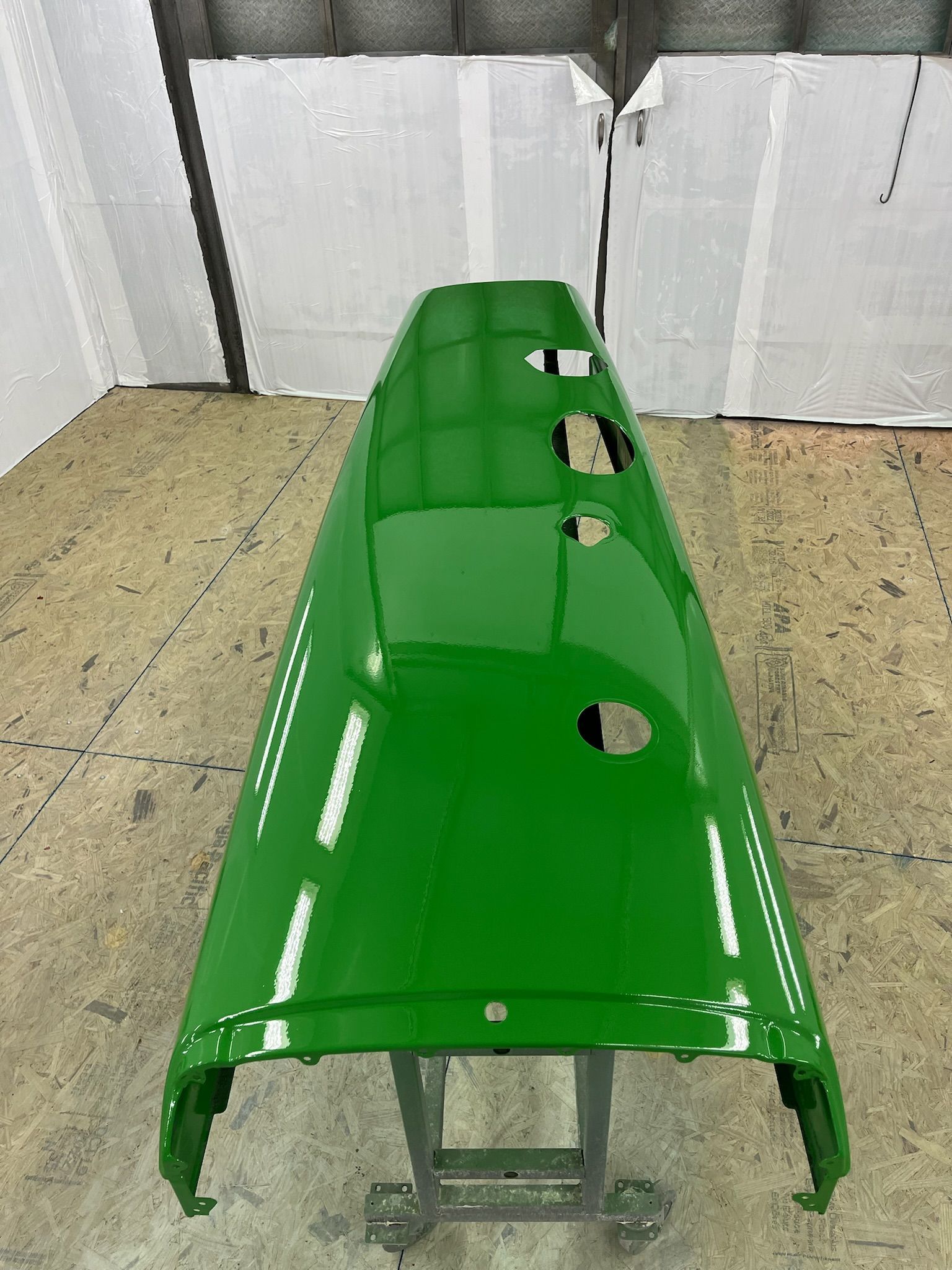 Green, freshly painted tractor roof on a metal stand. Three holes are visible on the top surface.