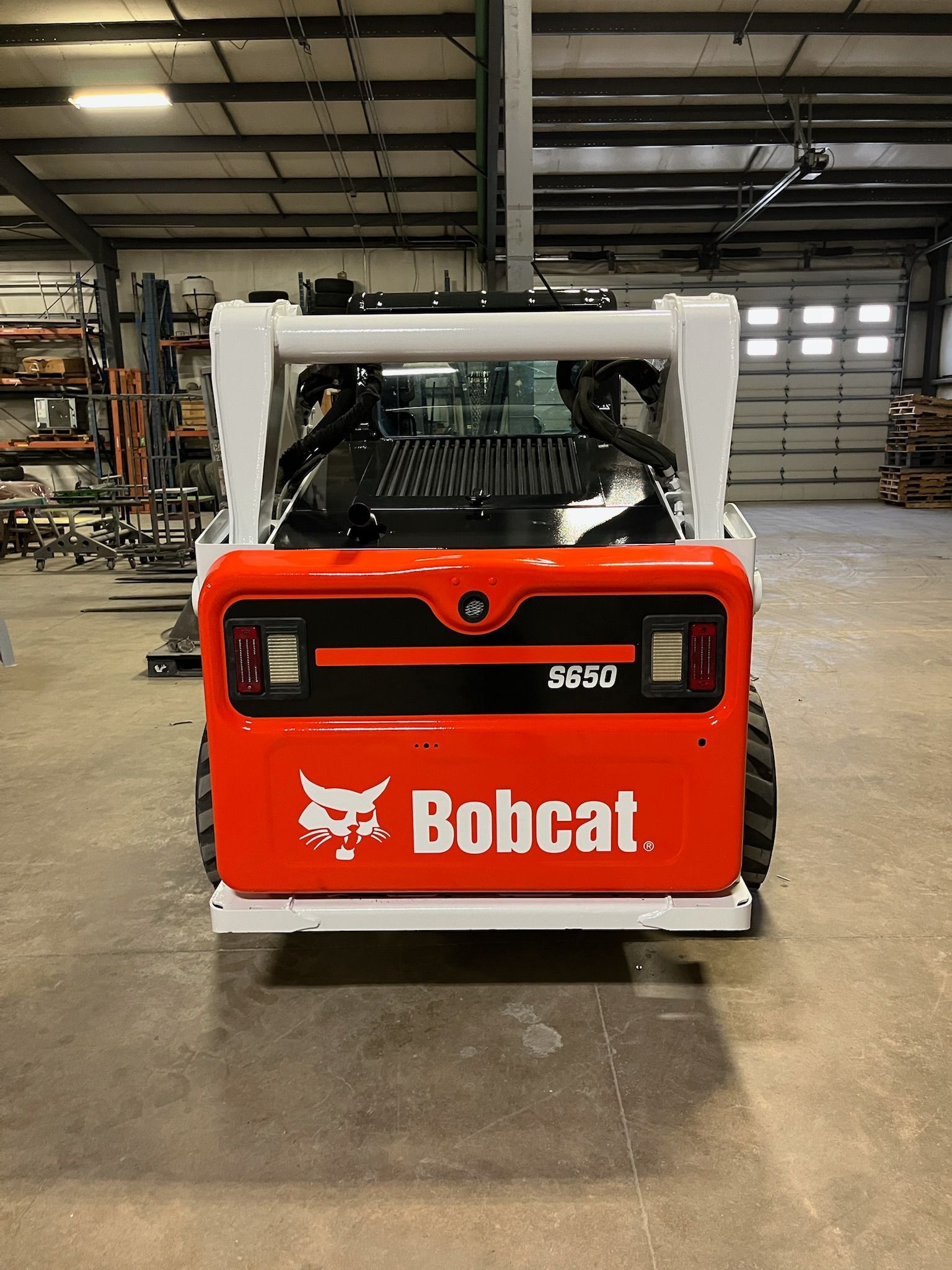 Rear view of an orange and white Bobcat E80 compact excavator in a warehouse setting.