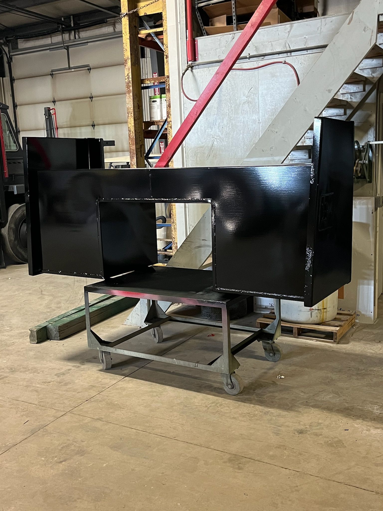 Black-painted metal structure with an opening, set on a rolling cart inside a workshop.