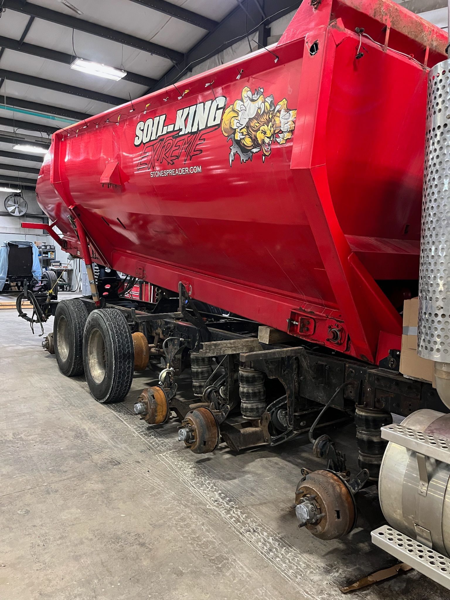 Red dump truck bed, partially disassembled, inside a repair shop.
