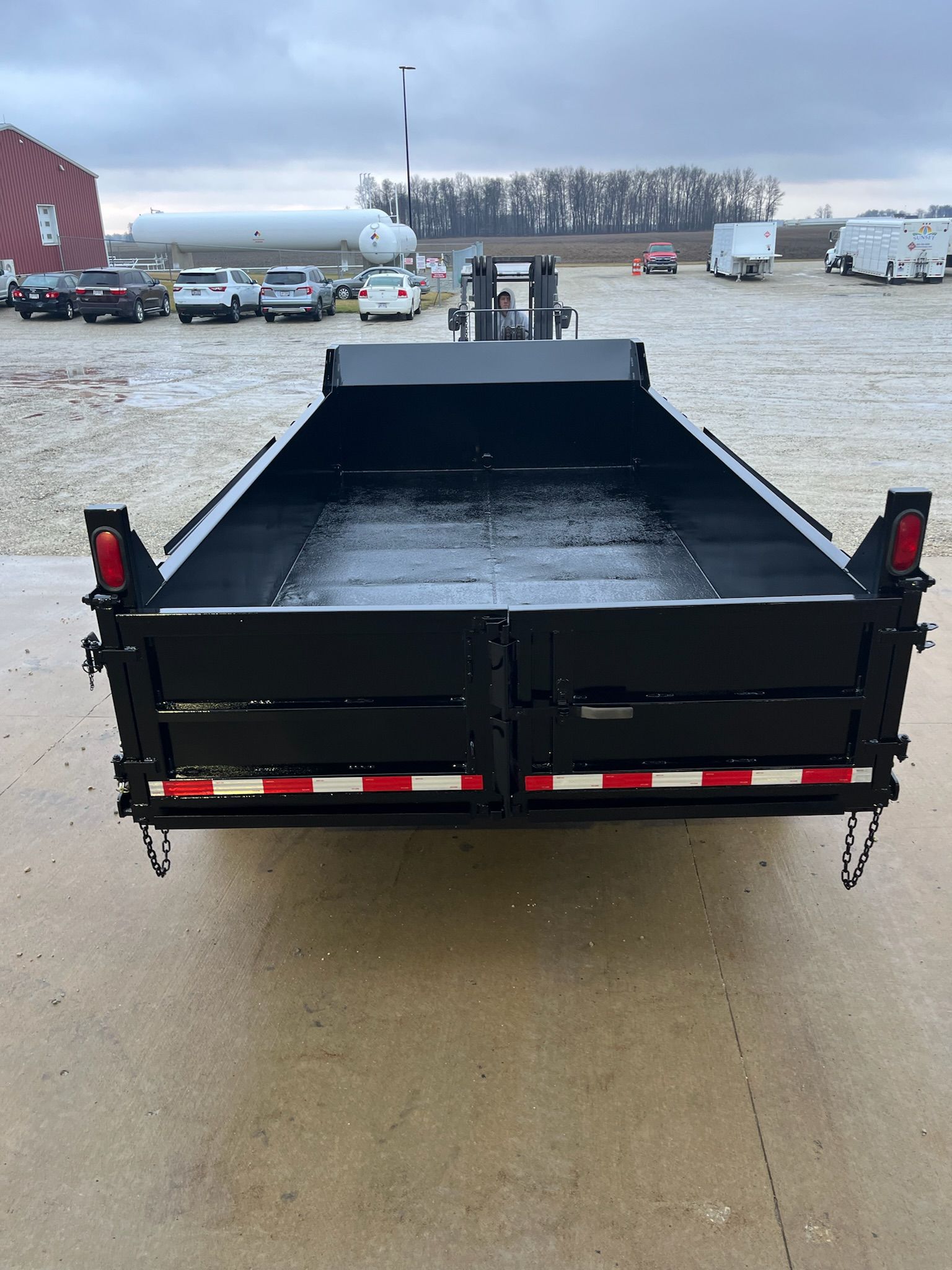 Black dump trailer with red and white reflectors, in a parking lot.