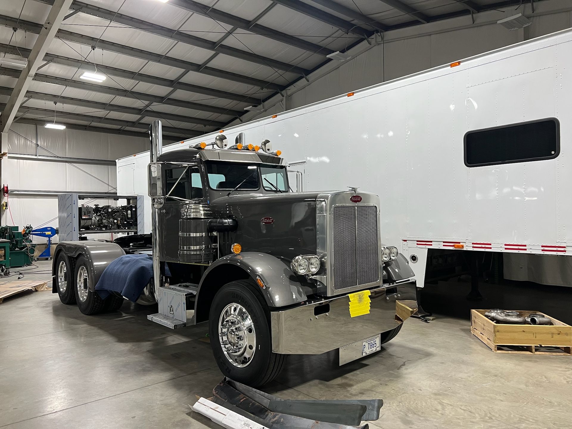 Gray semi-truck inside a garage with a white trailer, chrome details, and overhead lighting.