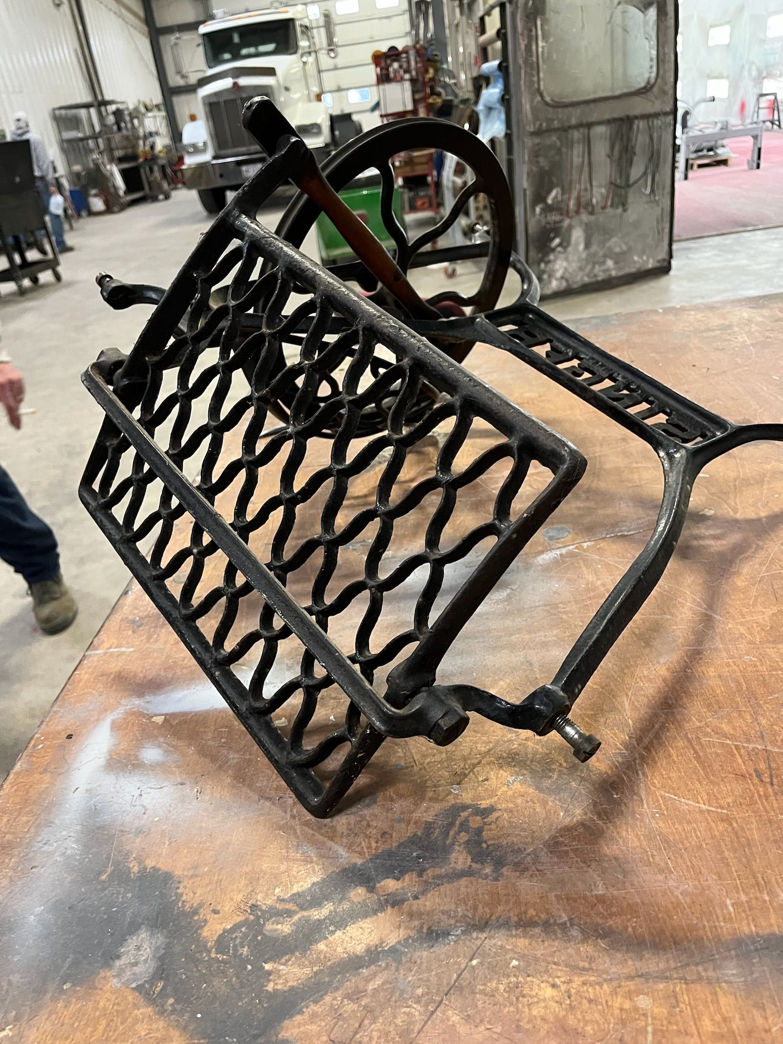 Black, ornate Singer sewing machine base on a workbench in a workshop.
