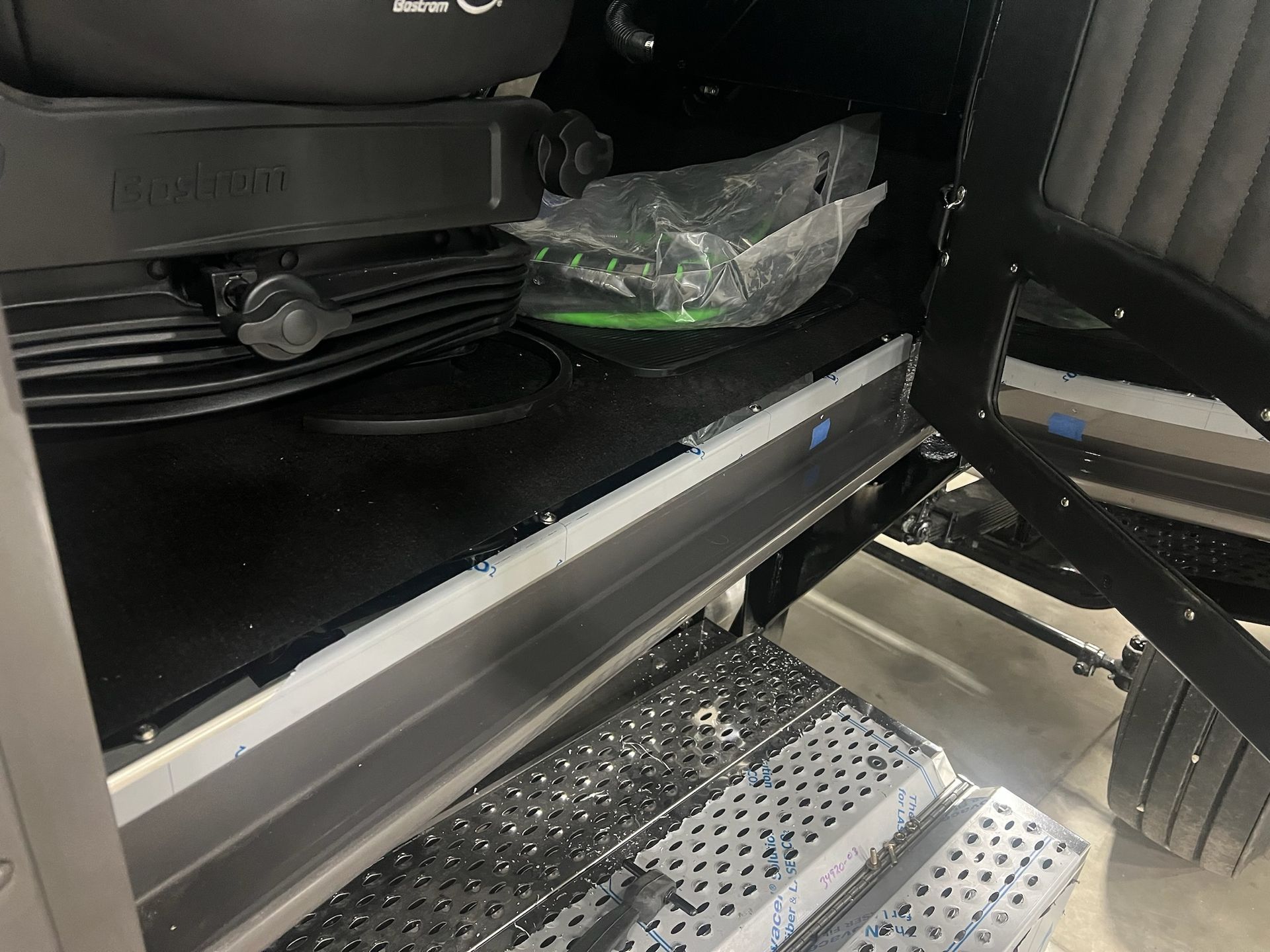 Interior view of a vehicle: black flooring, seat, and doorway. Silver trim and a metal step are visible.