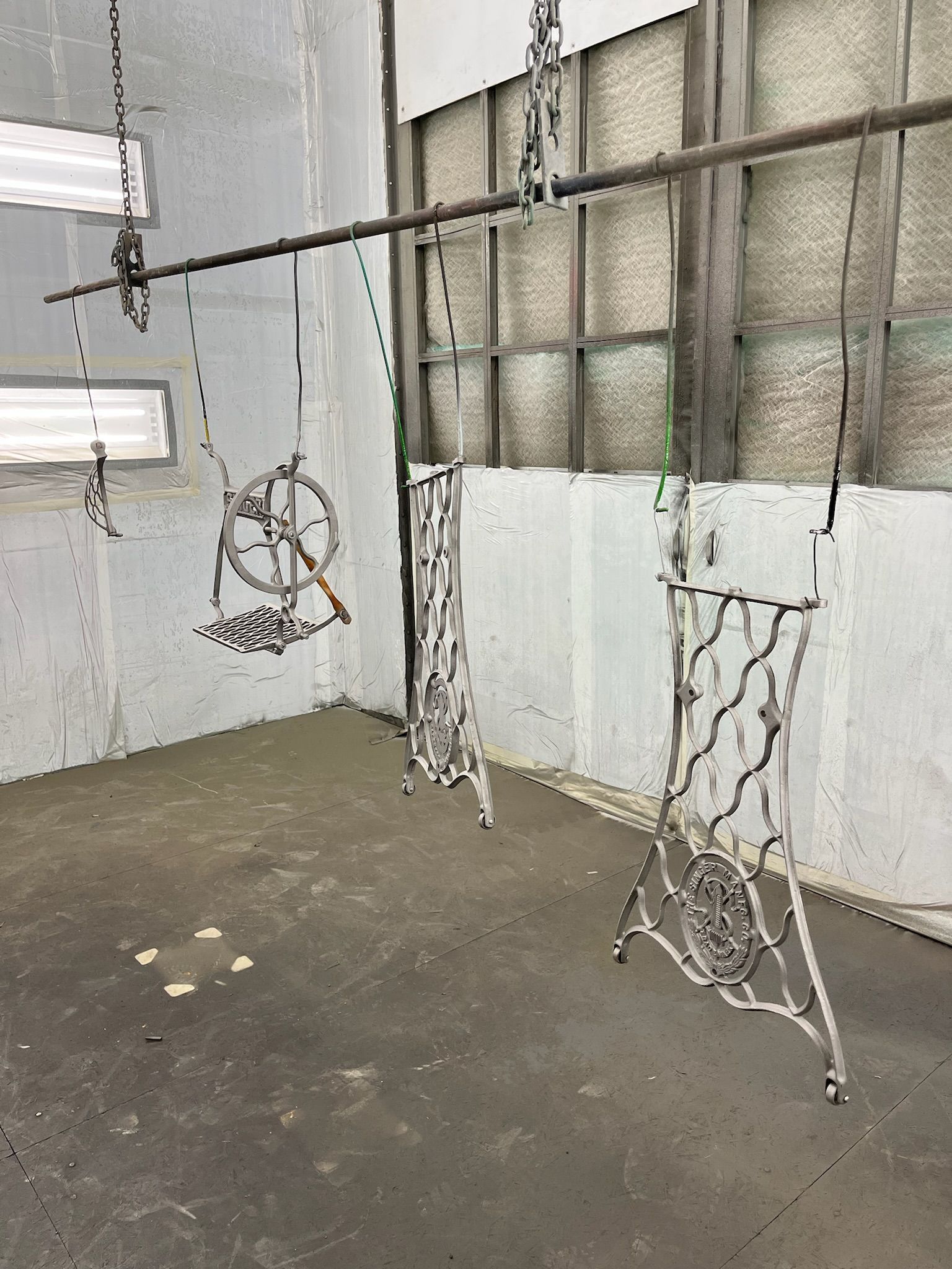 Metal sewing machine parts hanging in a workshop, ready for painting.
