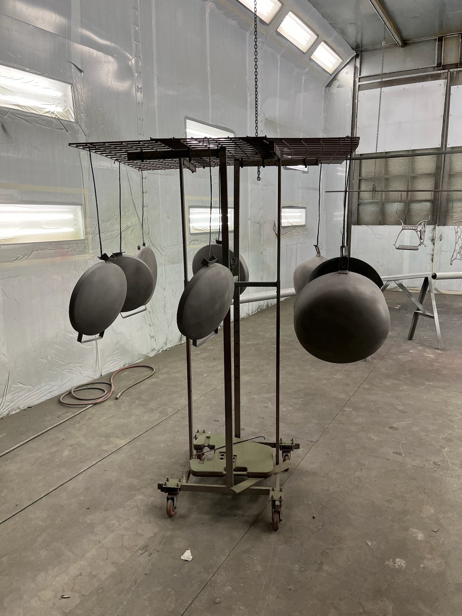 Parts painted gray hanging on a rotating rack in a spray booth.