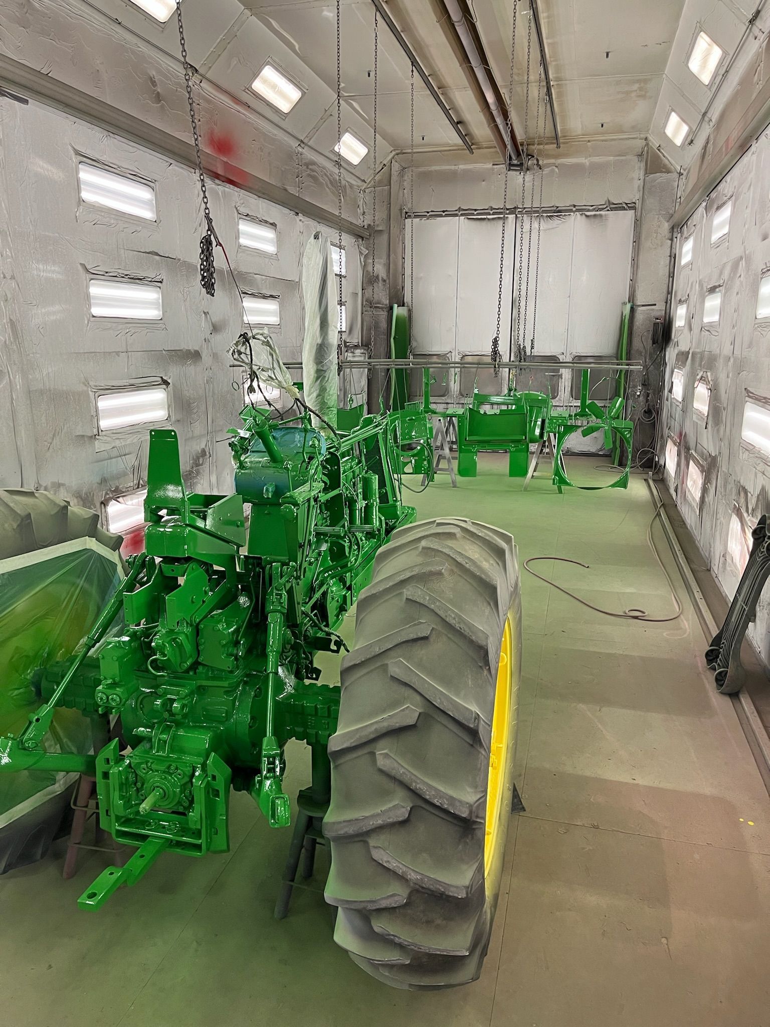 Green tractor and parts inside a paint booth with bright lights.