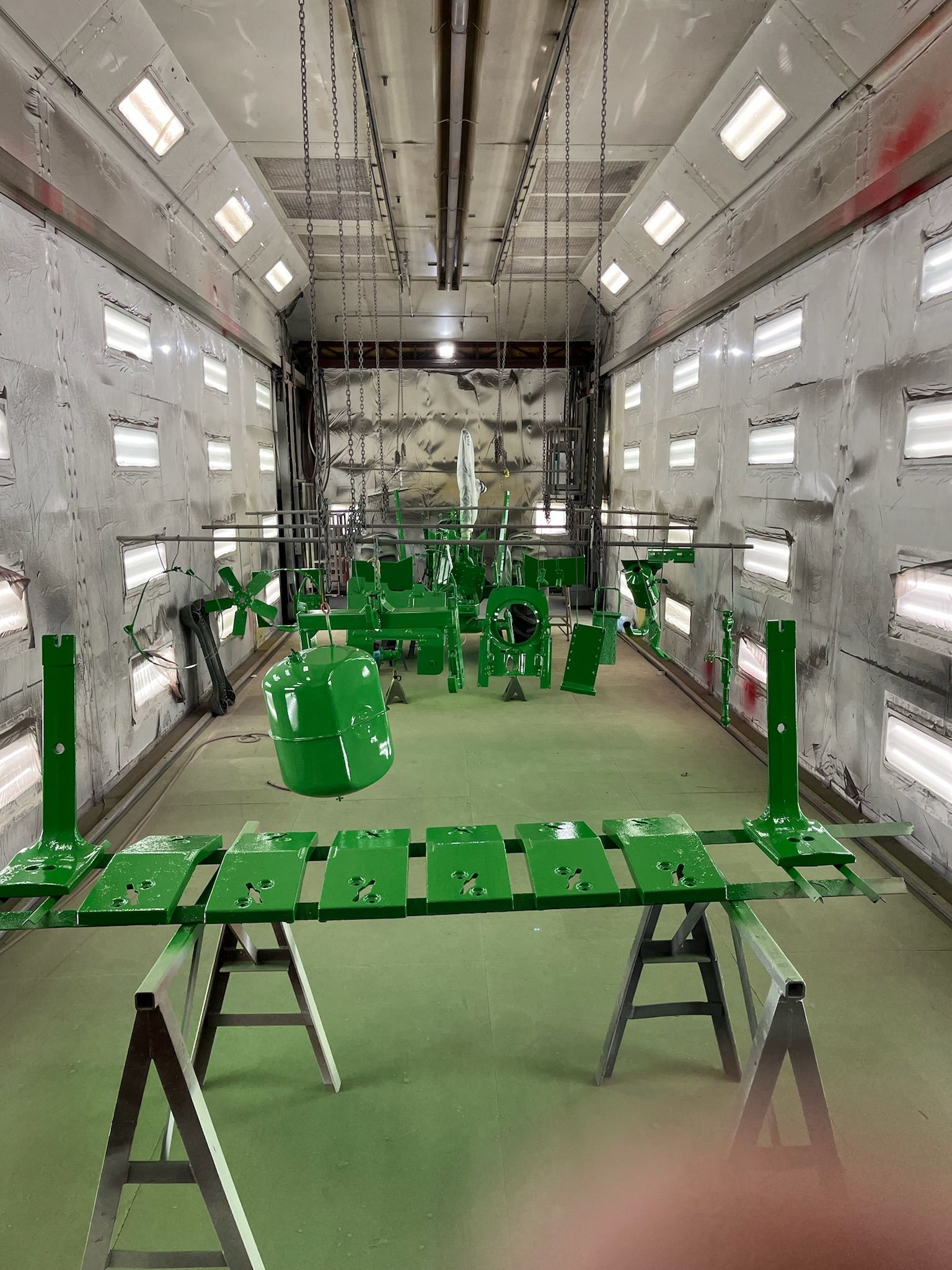 Green painted tractor parts inside an industrial paint booth with bright lights.