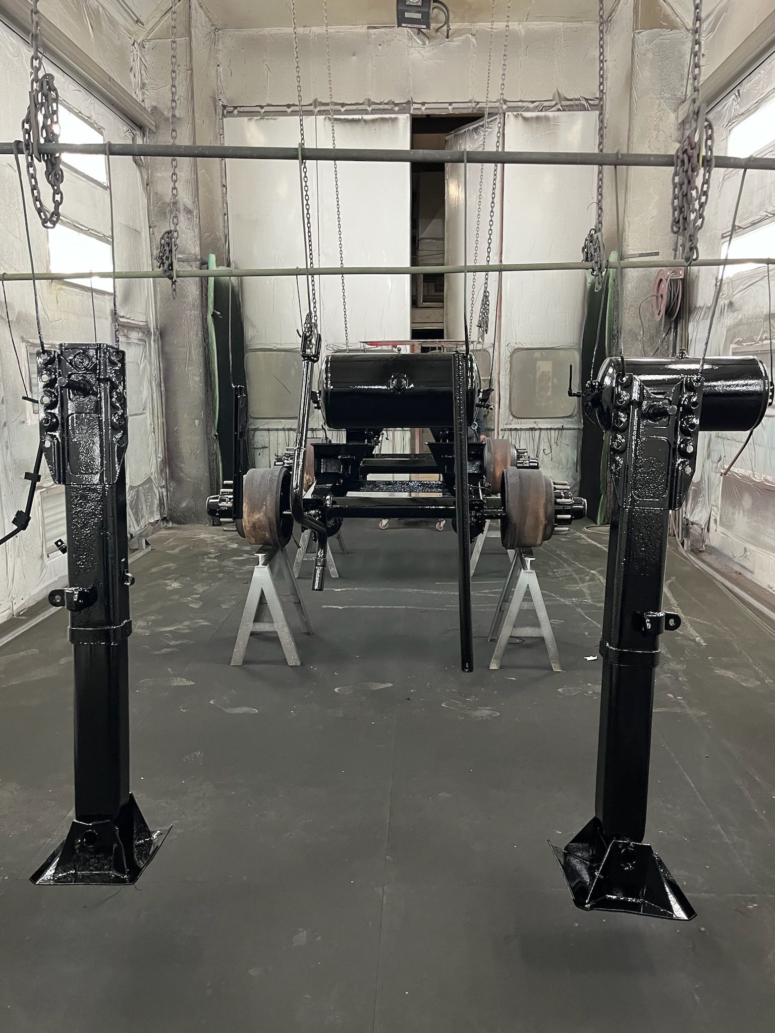 Black coated car chassis inside a spray booth. Two stands hold the chassis, parts suspended from overhead.