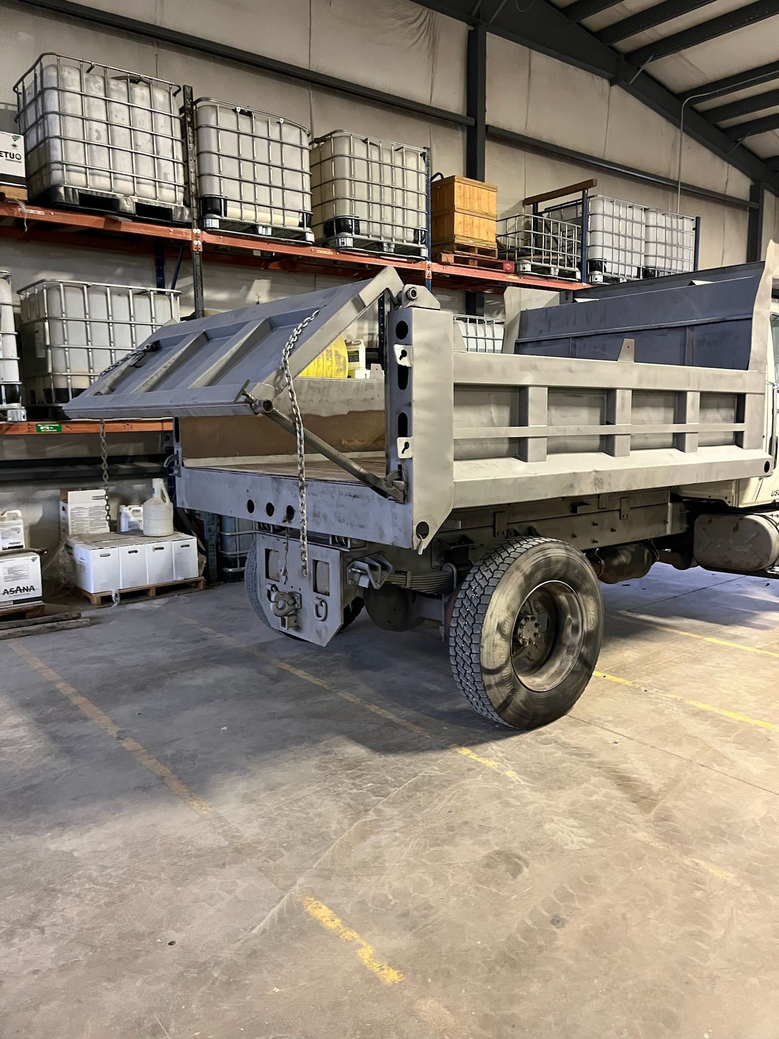 Gray dump truck in a warehouse with several large white containers.