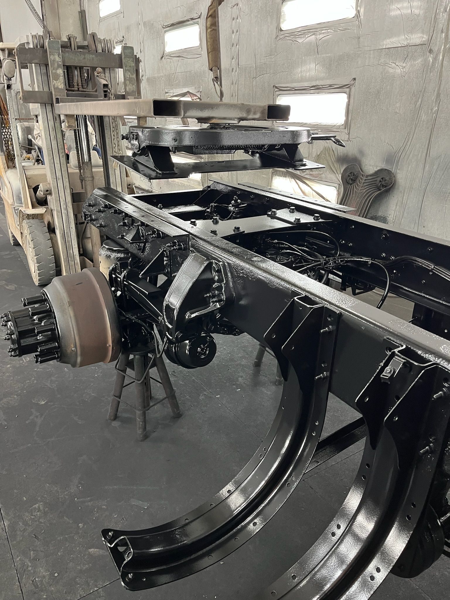 Black truck chassis in a workshop, possibly newly painted, near machinery.