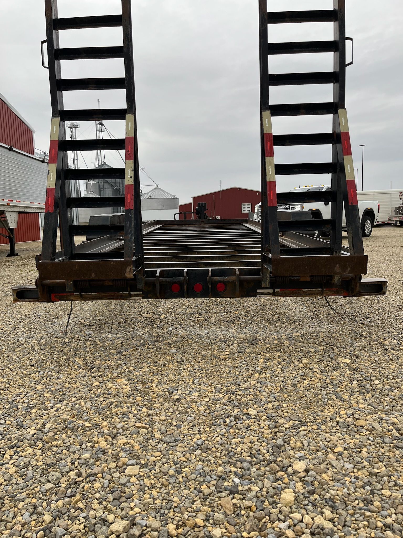 Heavy-duty trailer ramp with ladder-like sides on a gravel surface under a cloudy sky.