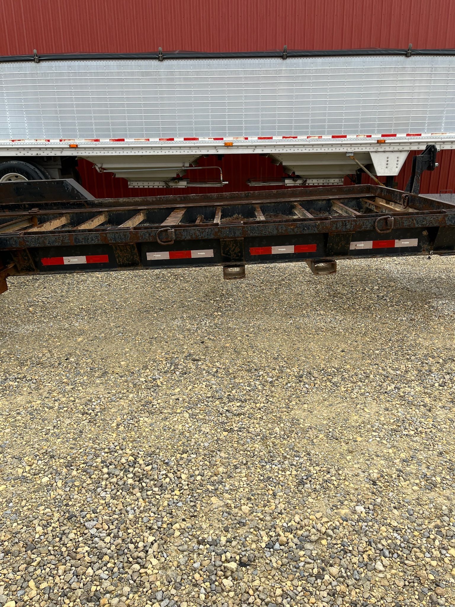 Lowboy trailer with black and red accents, parked on gravel.