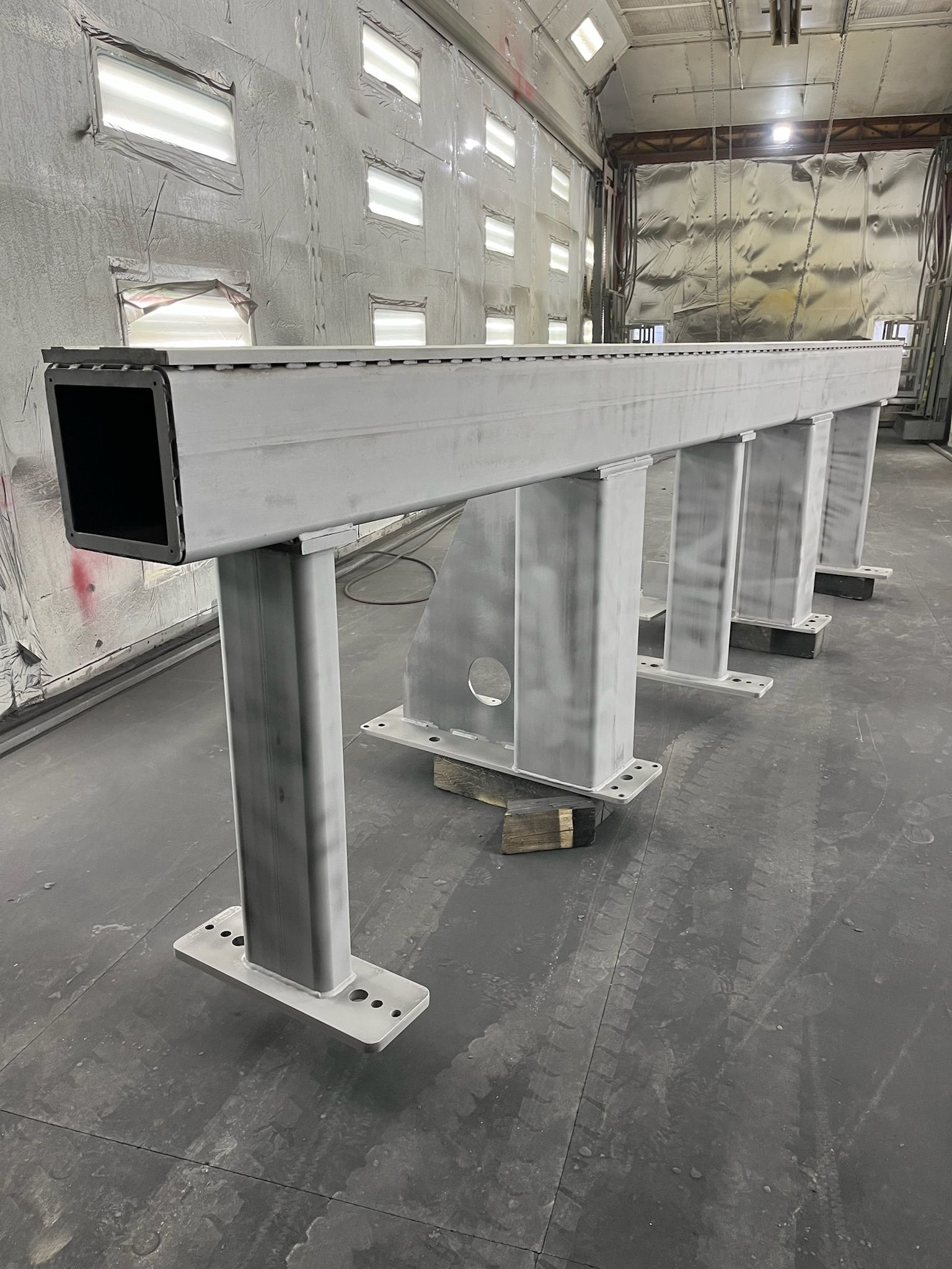 Gray metal industrial frame with a rectangular hollow beam supported by vertical pillars, in a warehouse.