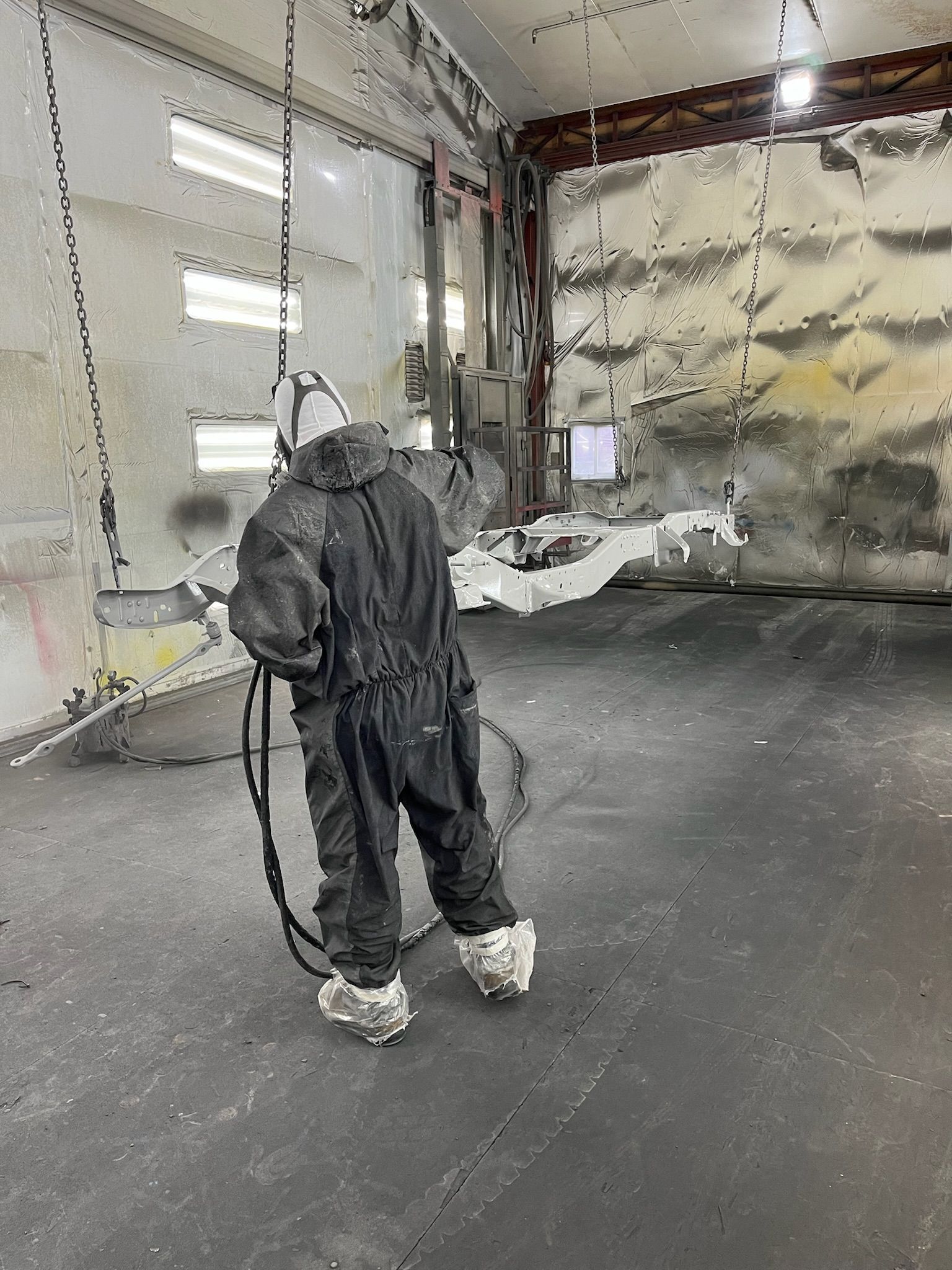 Person in protective suit sprays coating inside industrial building.