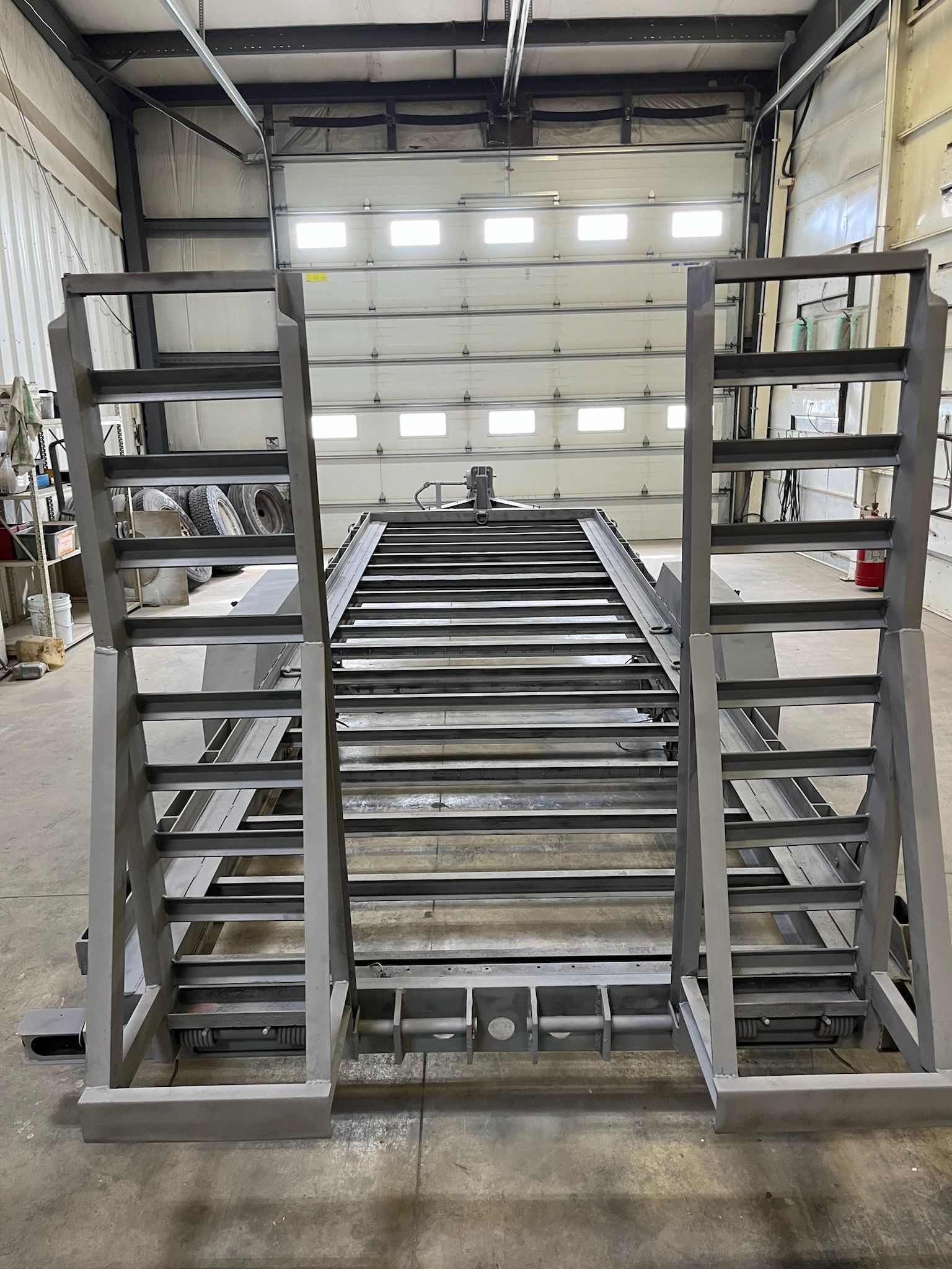 Gray metal structure with ladder-like sides and a central platform, likely industrial equipment, in a workshop setting.