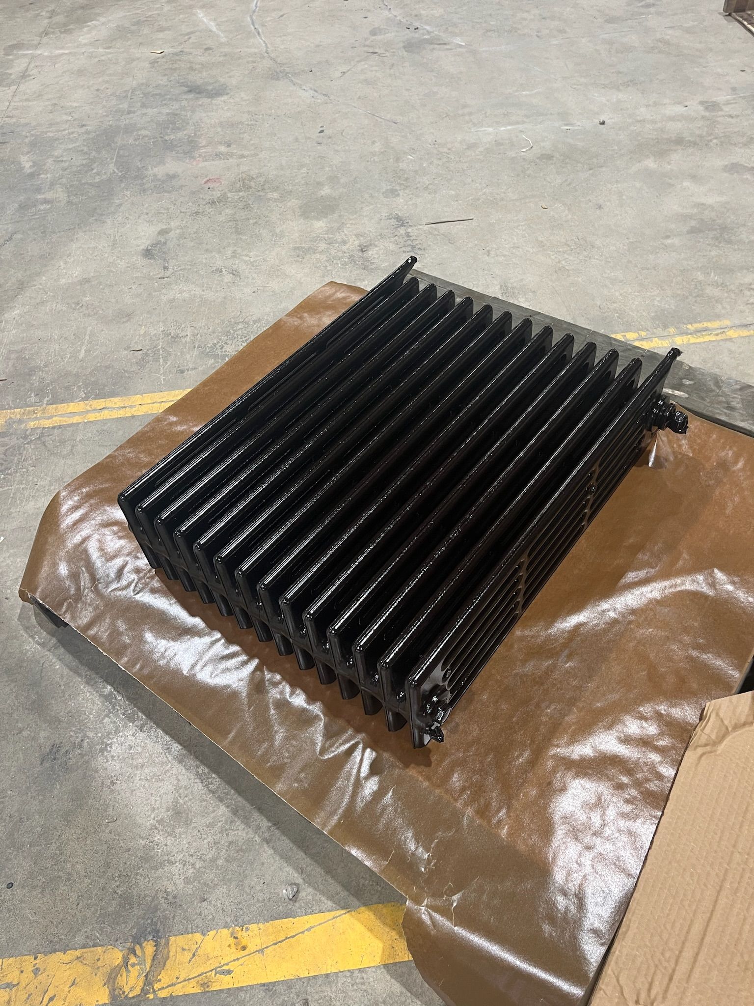 Black-painted radiator on brown paper, resting on a concrete floor.