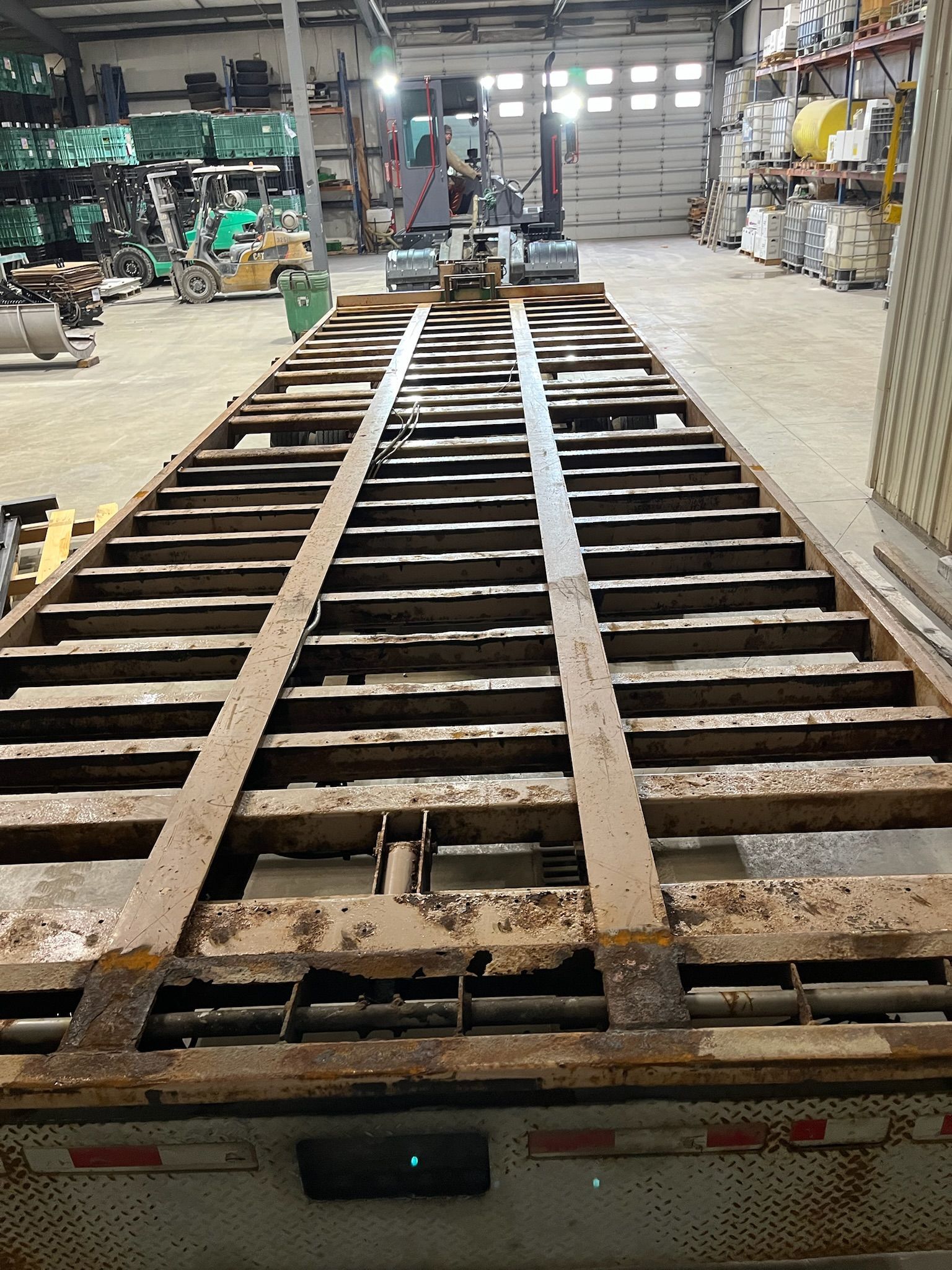 A rusty flatbed trailer inside a warehouse, viewed from the front.