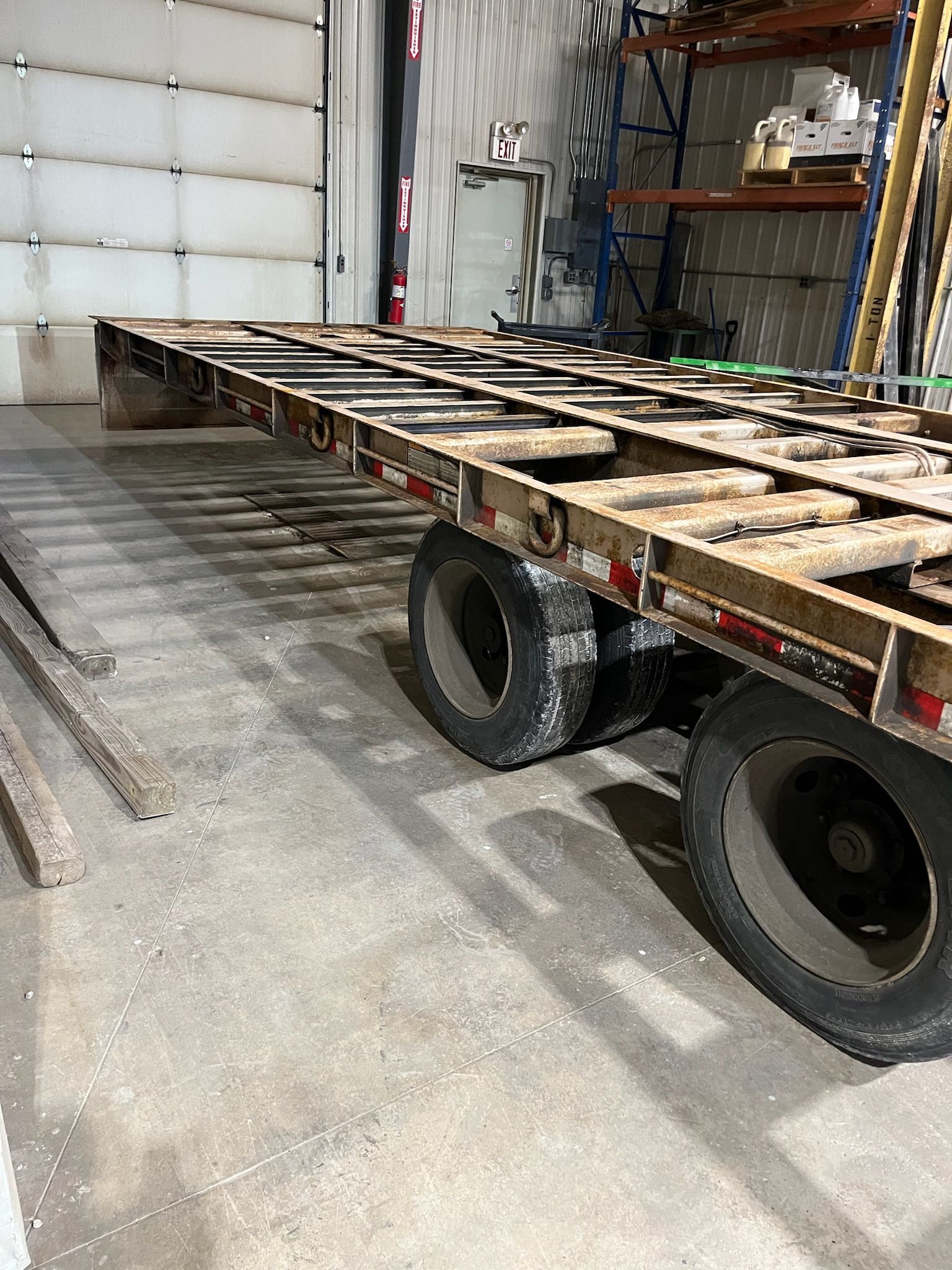 Empty flatbed trailer with two tires, in a warehouse.