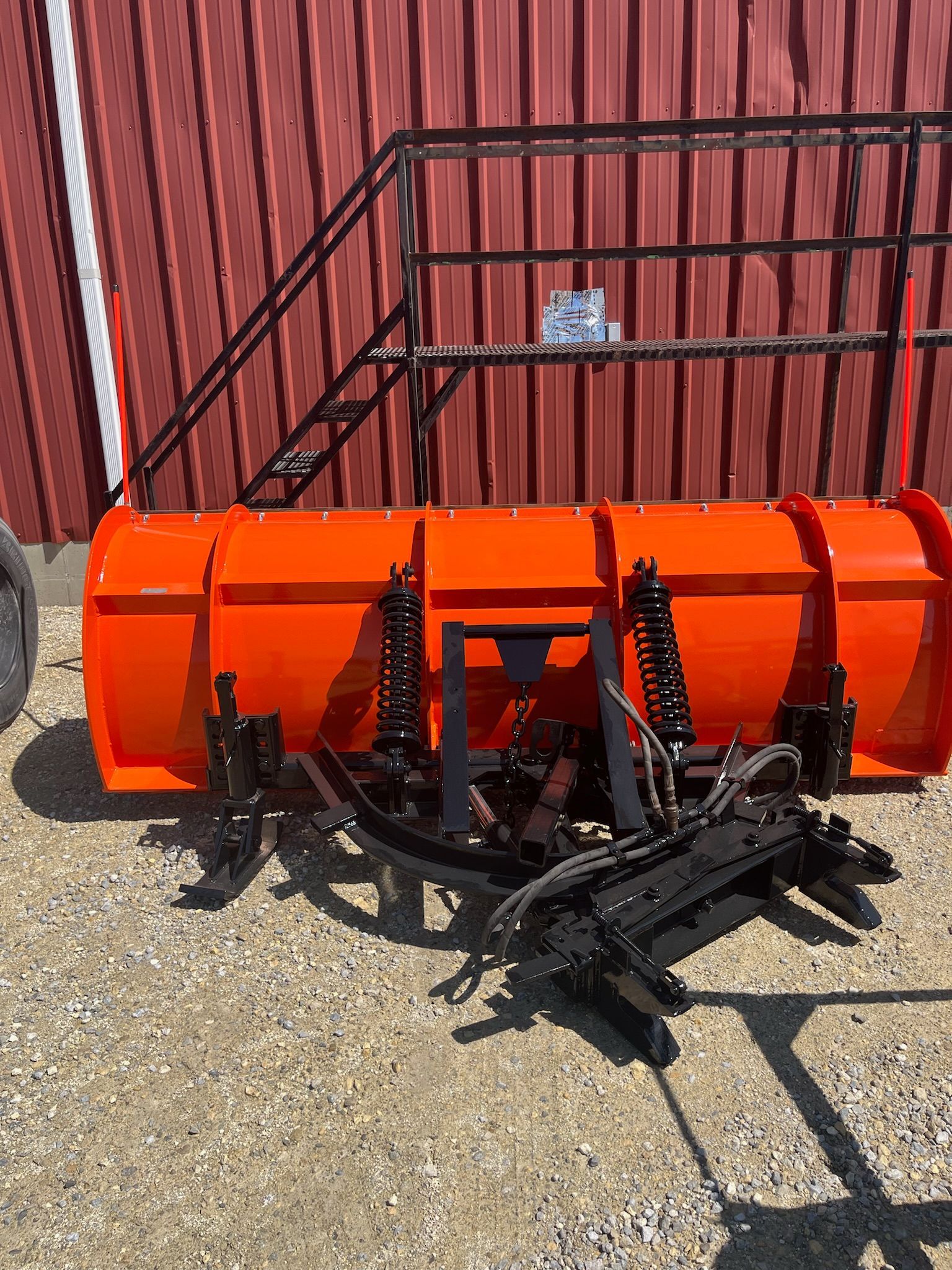 Orange snow plow with black frame, leaning against a red barn.