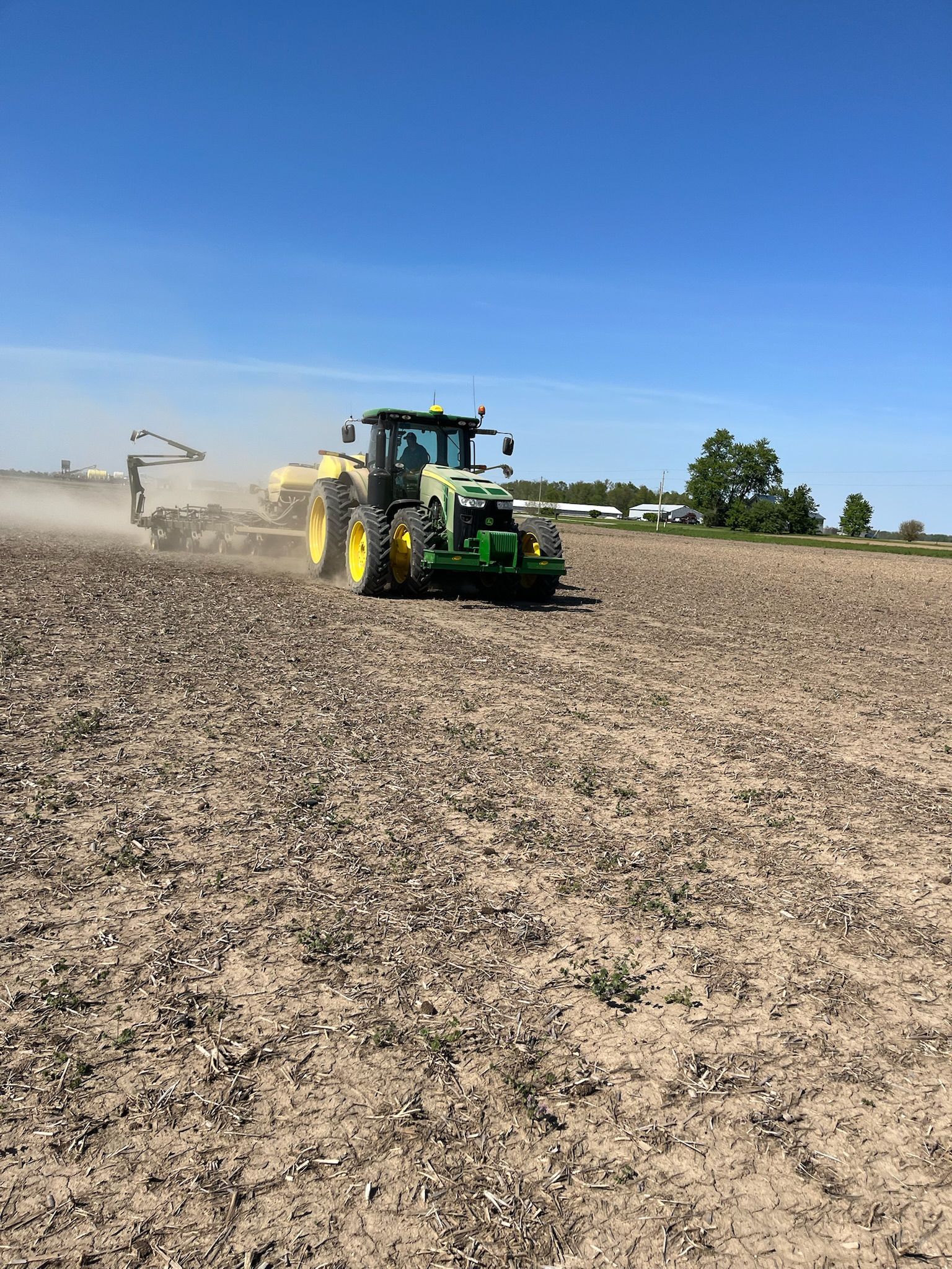 Green tractor planting seeds in a field on a sunny day.