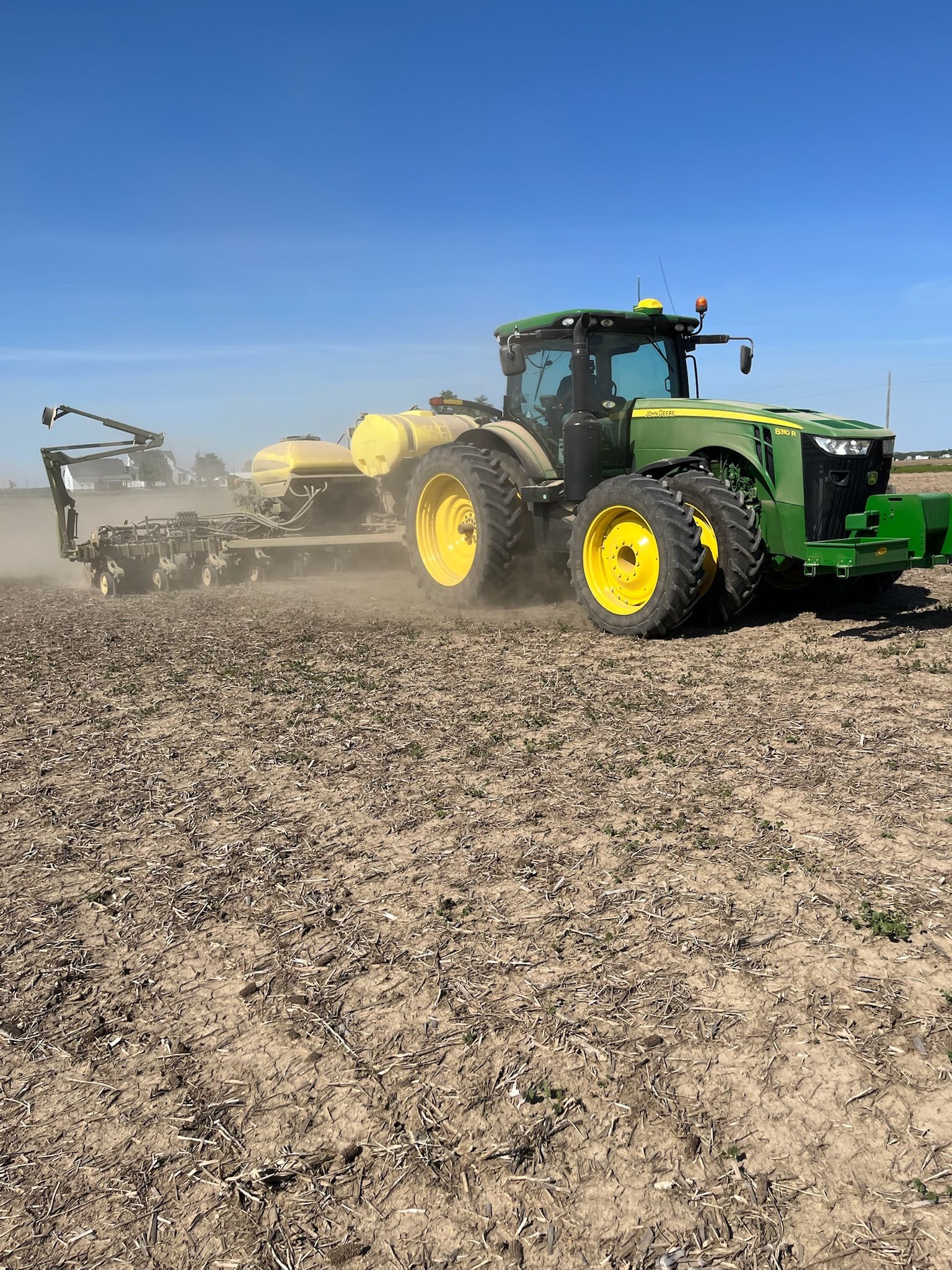 Green and yellow John Deere tractor planting seeds in a field under a clear blue sky.