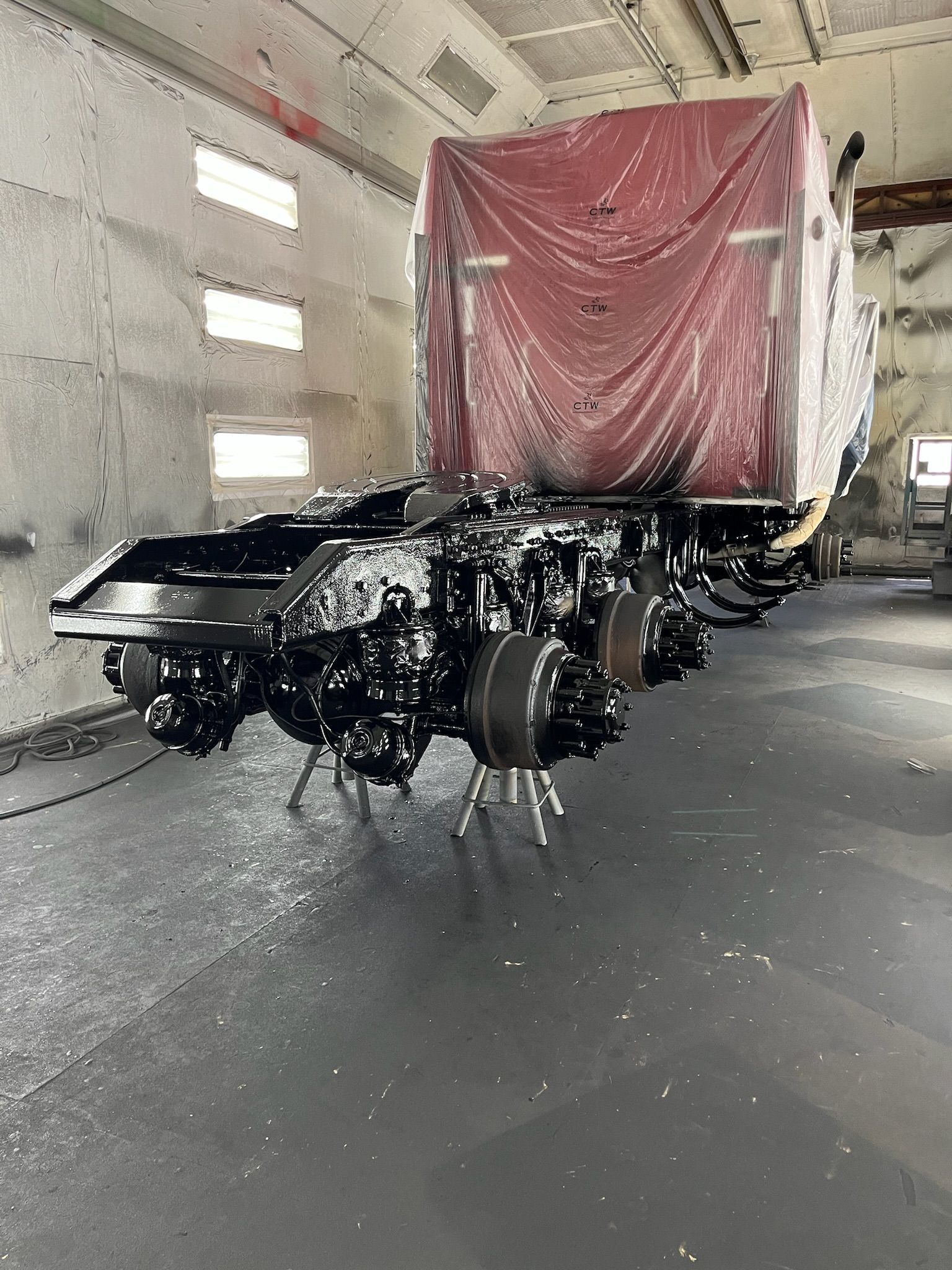 Black truck chassis in a spray booth with red-covered cab.