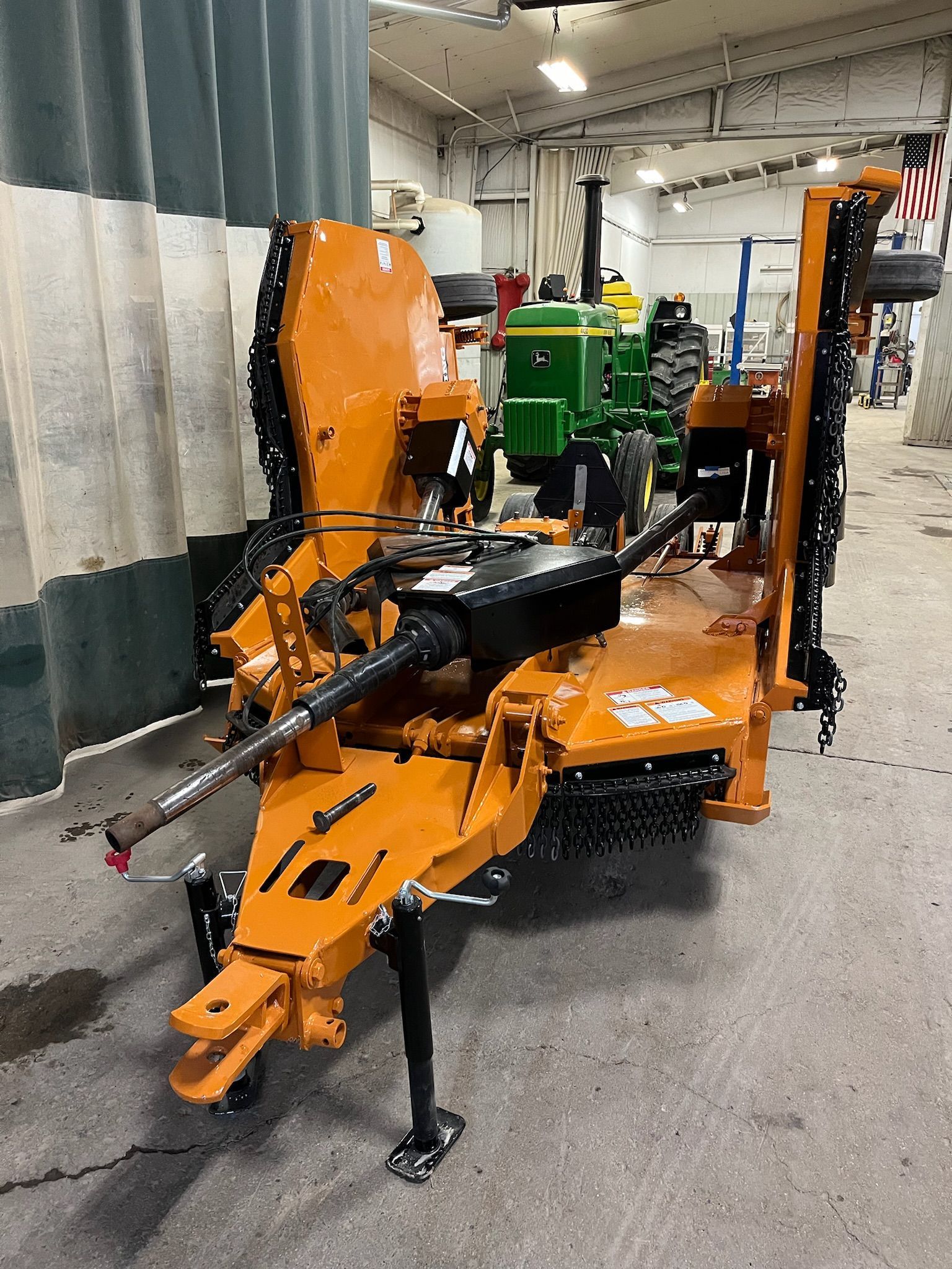 Orange agricultural mower with a John Deere tractor in a building.