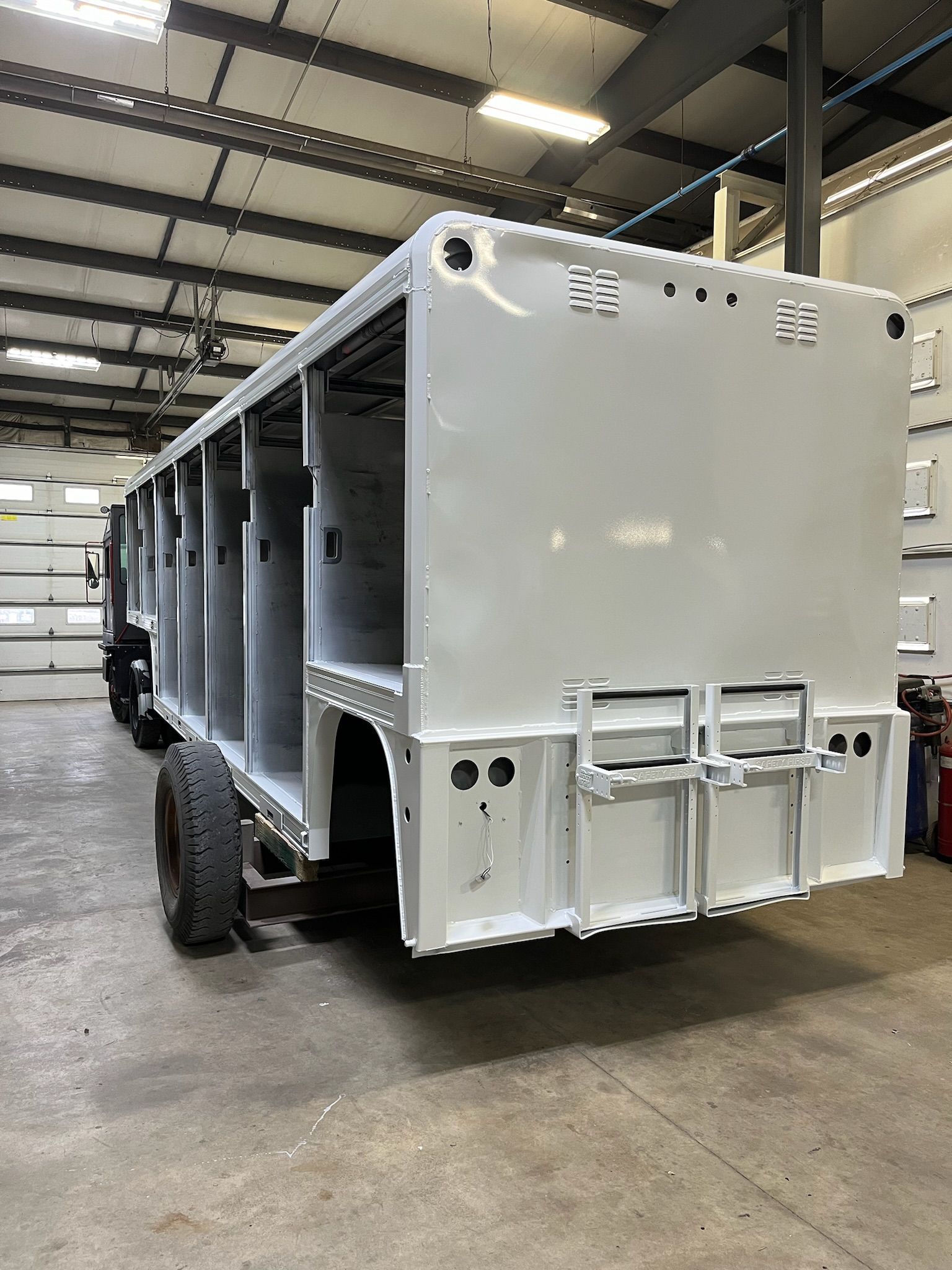 A gray truck frame, with open compartments, sits in a shop.