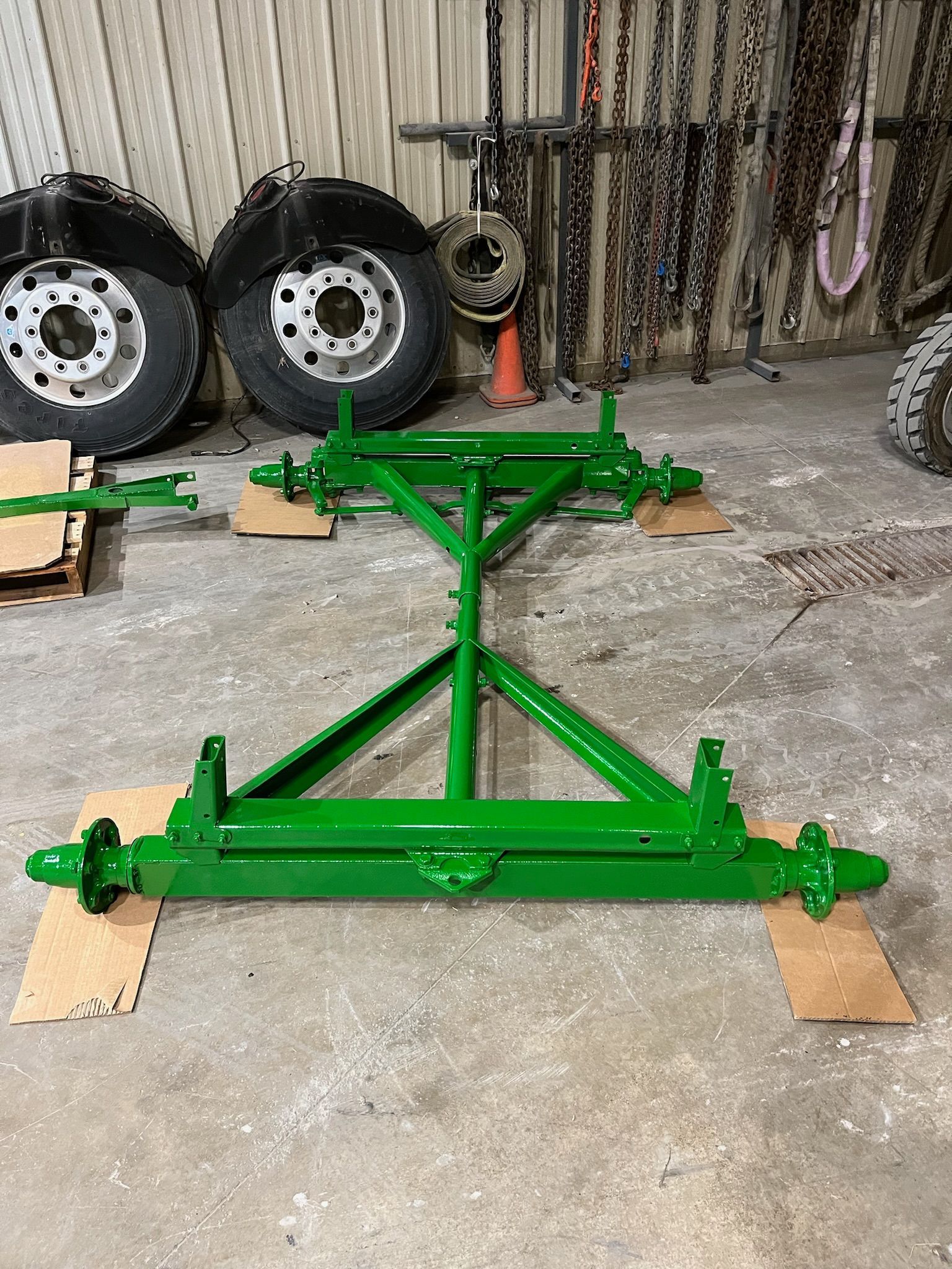 Green painted farm equipment frame, likely a trailer. Two tires in background.