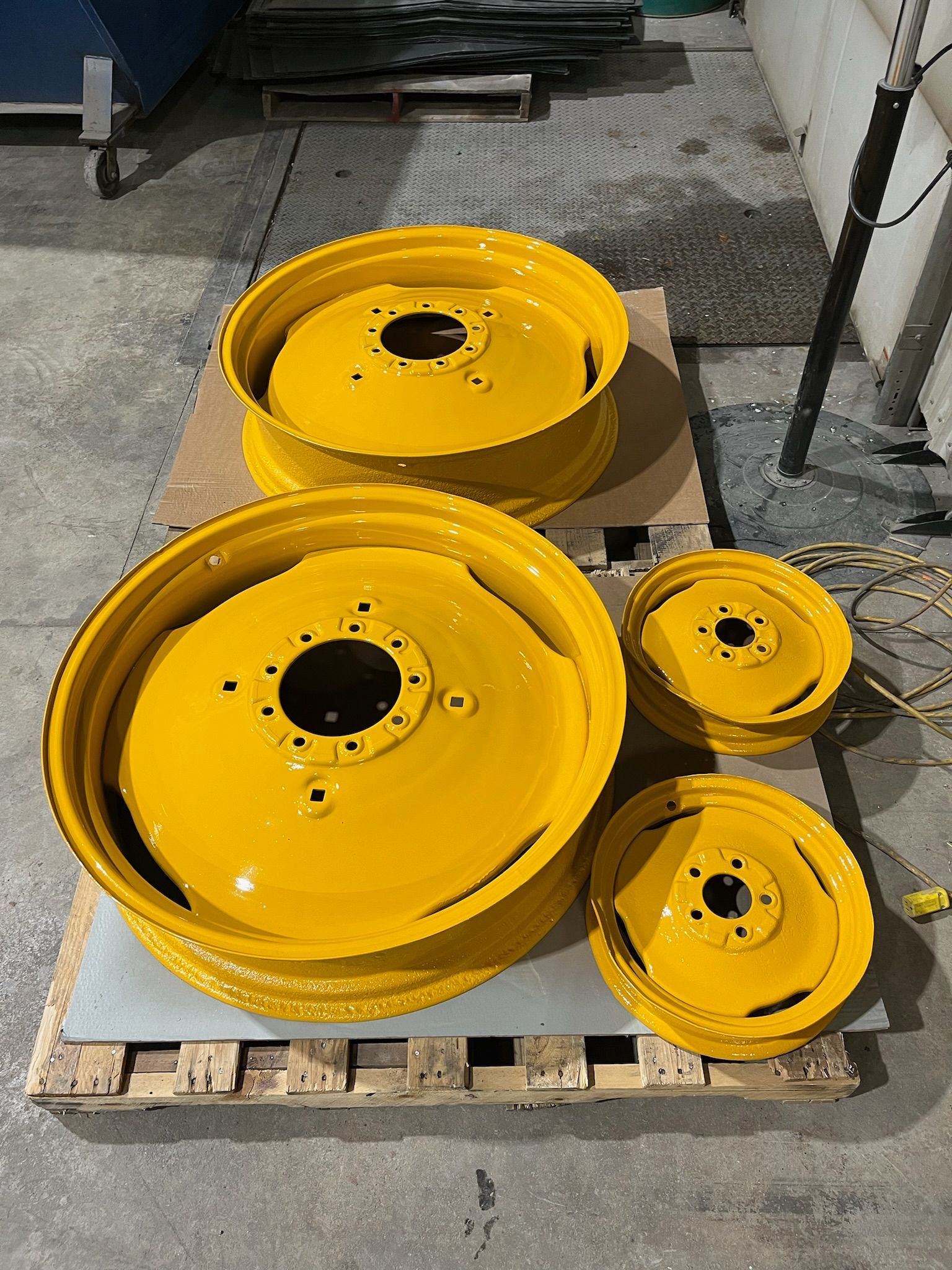 Four yellow tractor wheels on a wooden pallet in a workshop setting.
