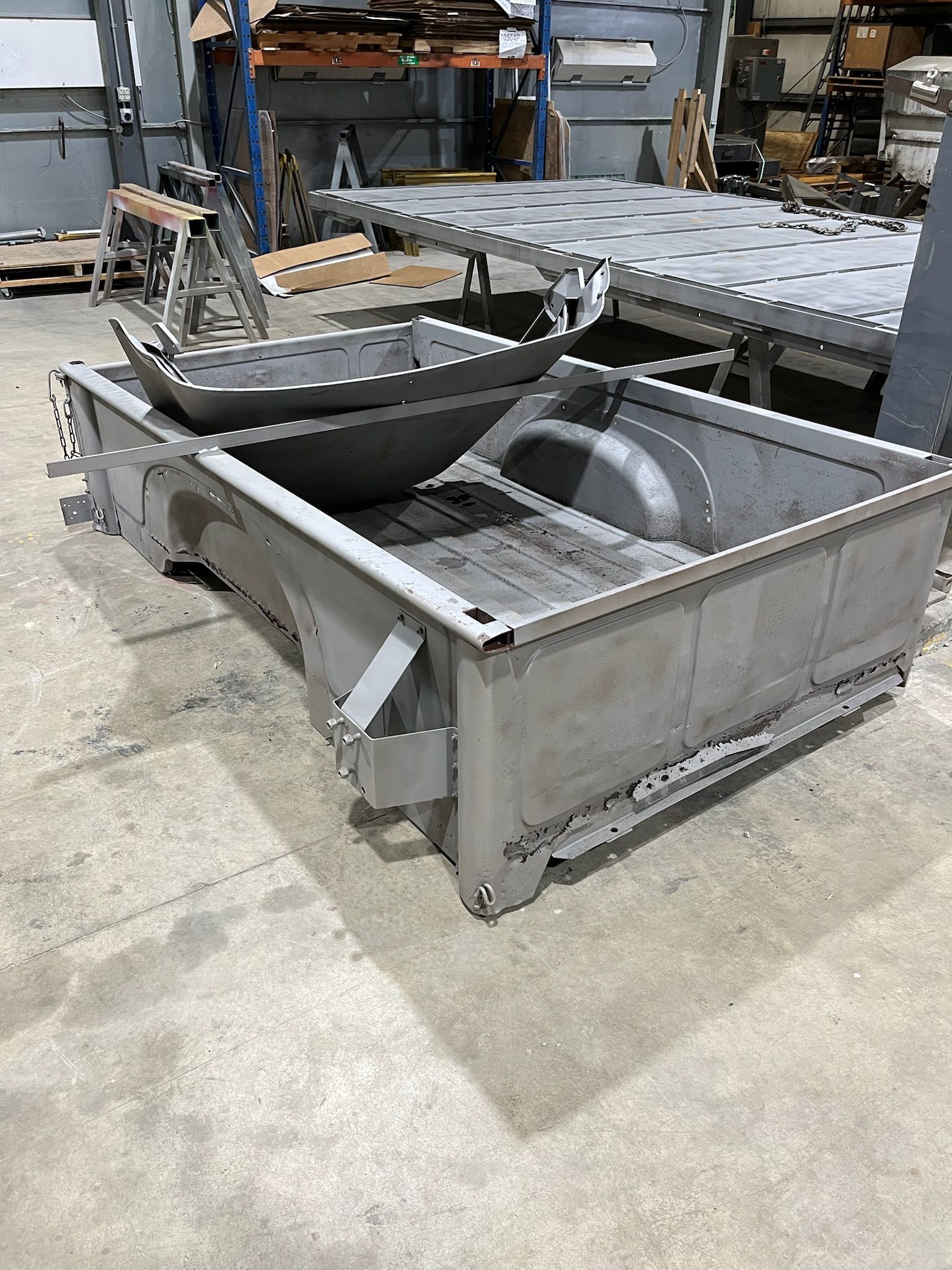 Metal truck bed and parts in a workshop, possibly for fabrication.