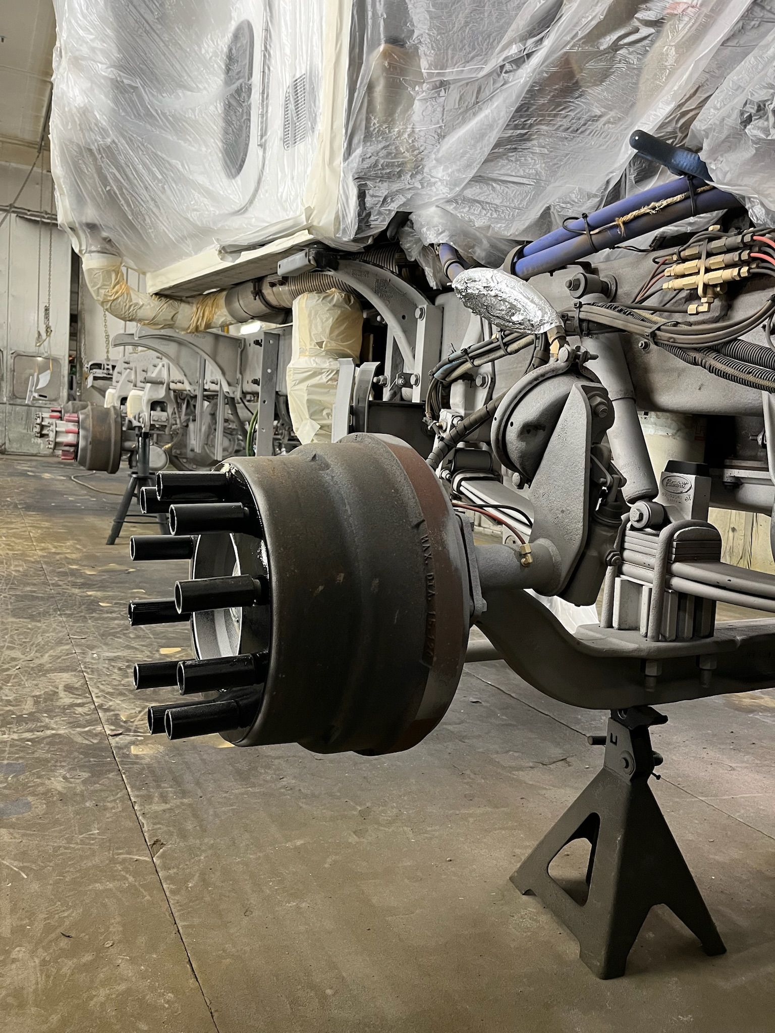 Truck axle on jack stands in a garage; drum brake assembly visible, truck undercarriage.