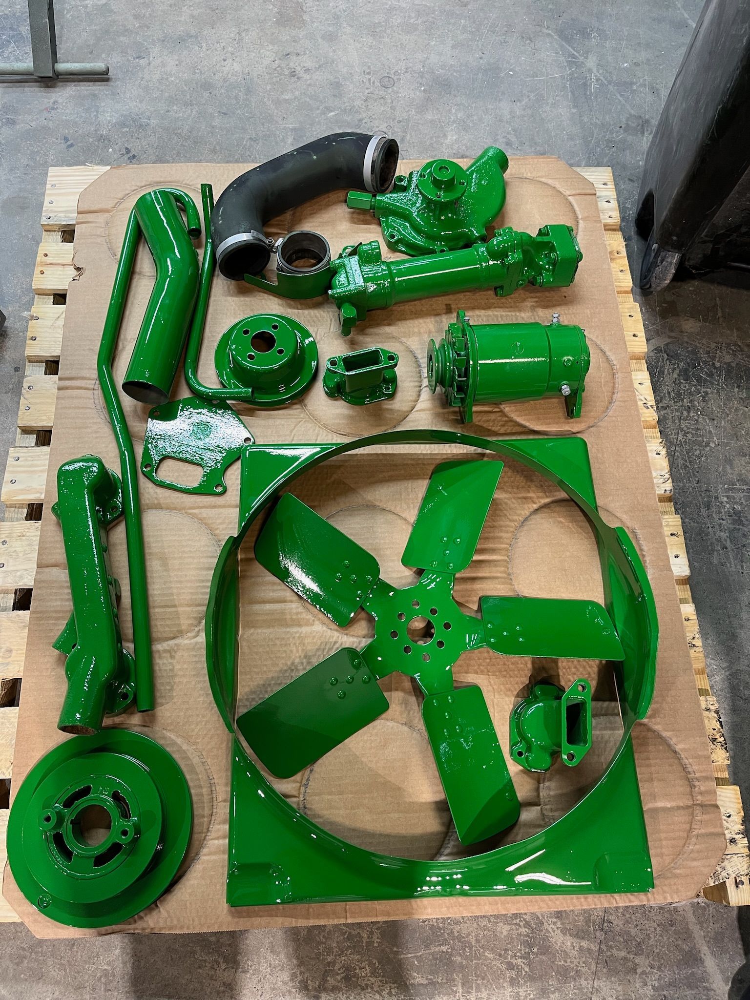 Green tractor parts, freshly painted and arranged on a wooden pallet.