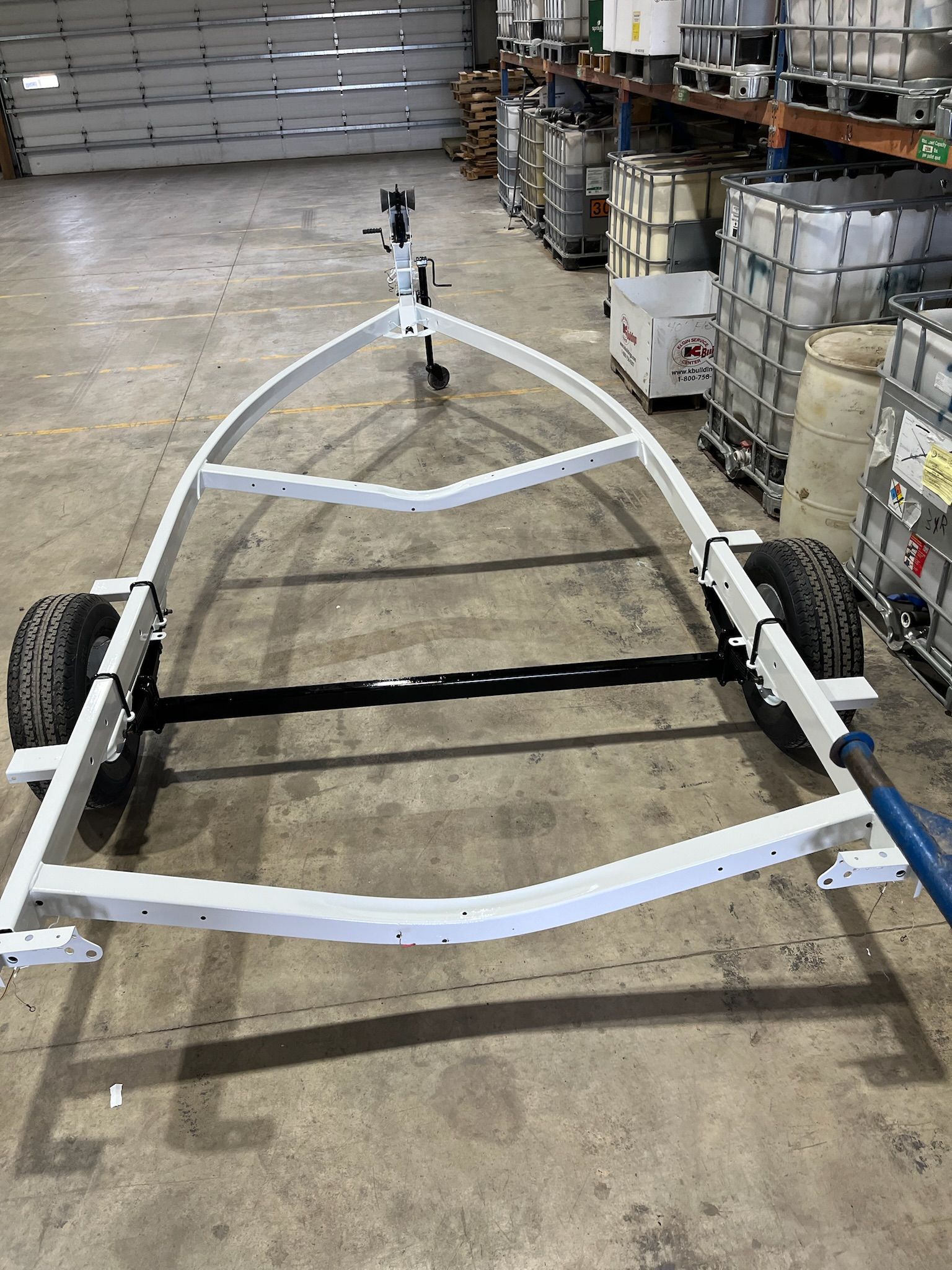 White boat trailer on a concrete floor in a warehouse, with black tires and supporting beams.