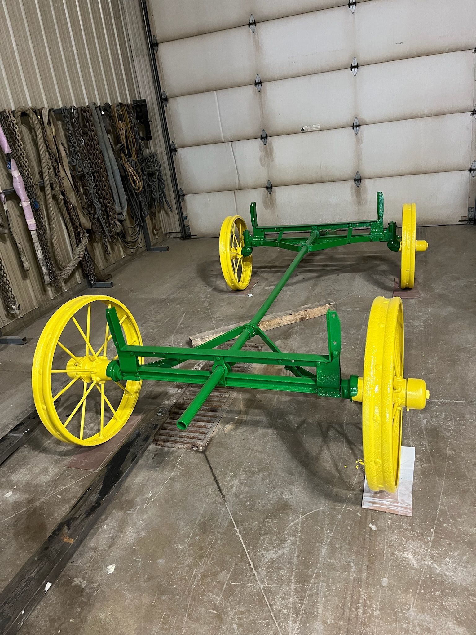 Two green and yellow farm implement wheels and frames, likely for a wagon, sit on a concrete surface.