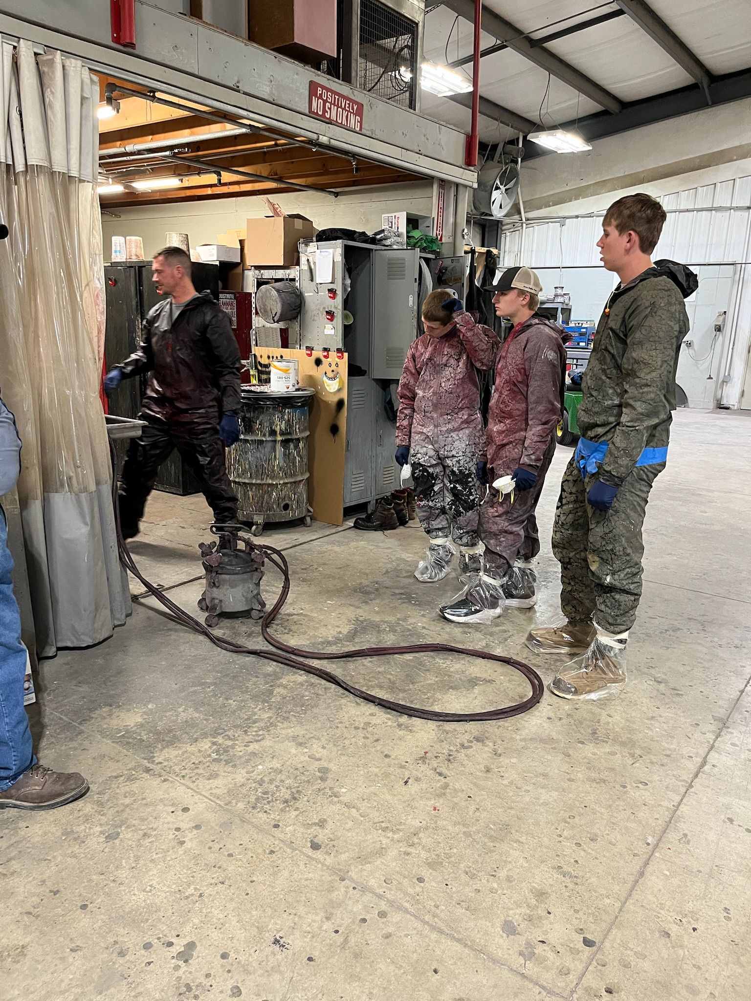Four people in a workshop observing a machine. One operates it, while others watch.