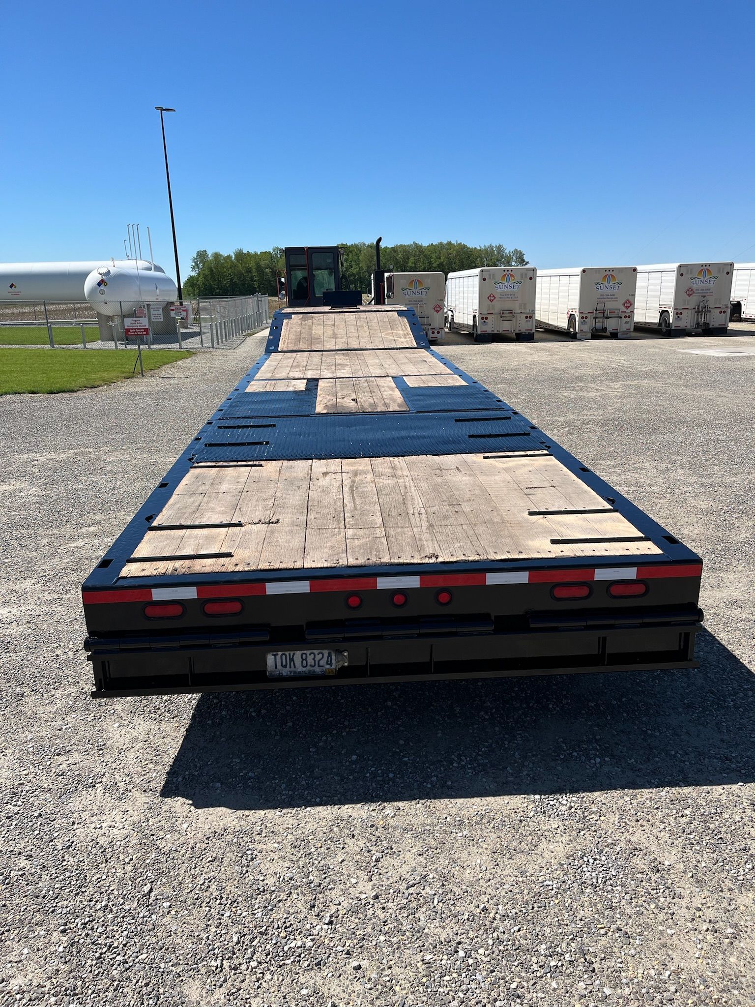 Flatbed trailer on gravel, at an airport, with an excavator and equipment in background.