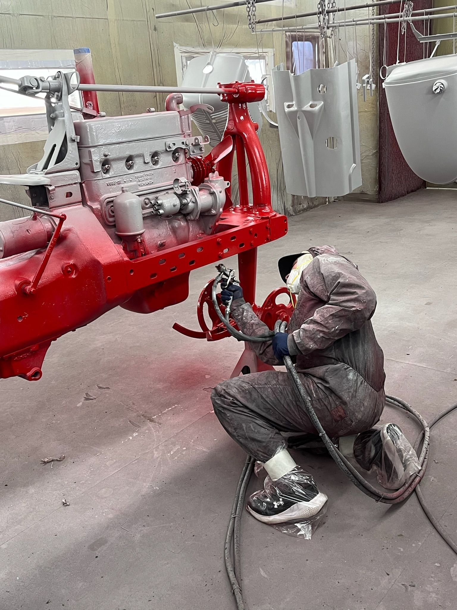 Person in a jumpsuit spray painting a red vehicle frame with an engine attached.