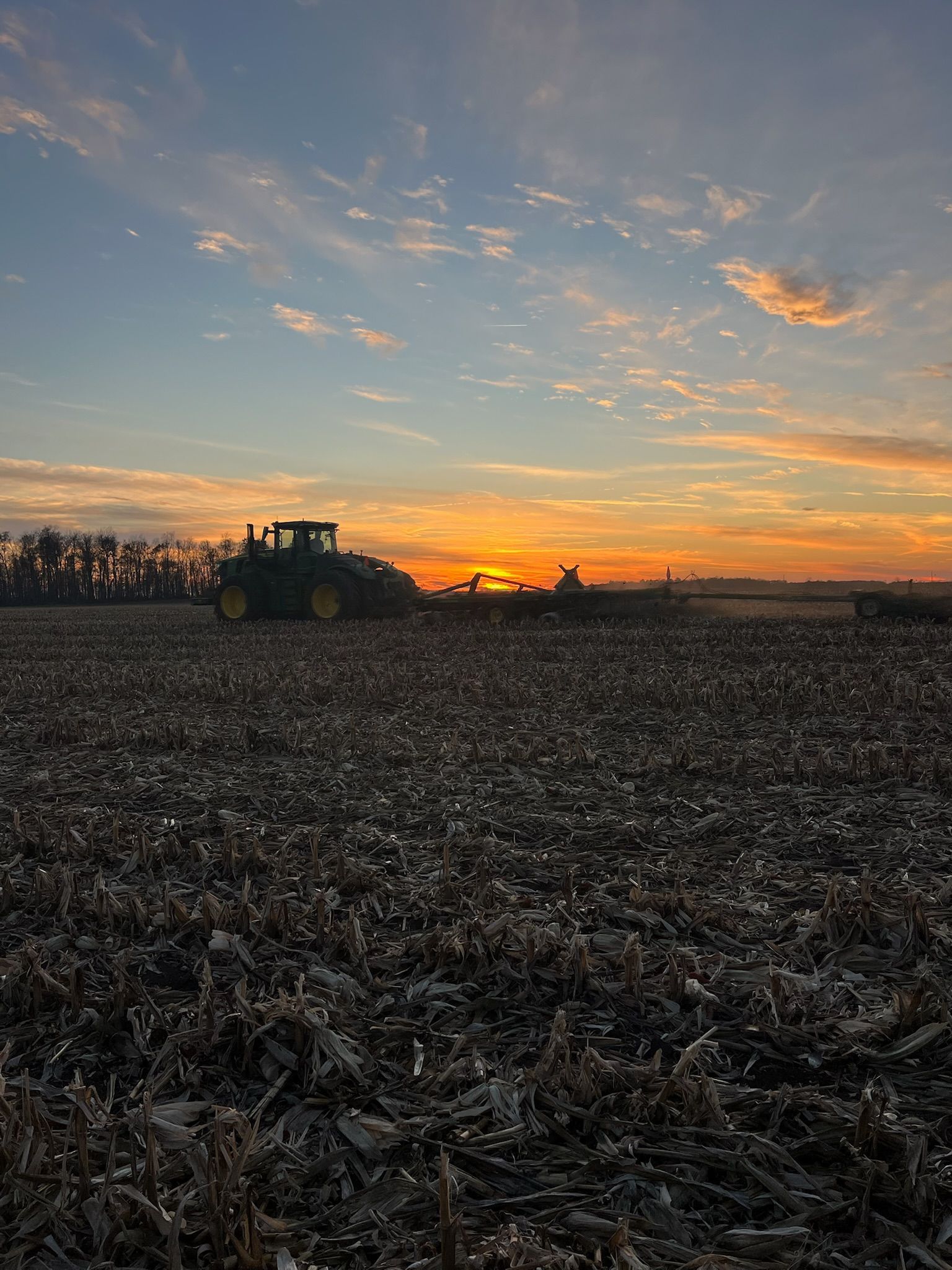 Tractor plowing a field at sunrise with a colorful sky.