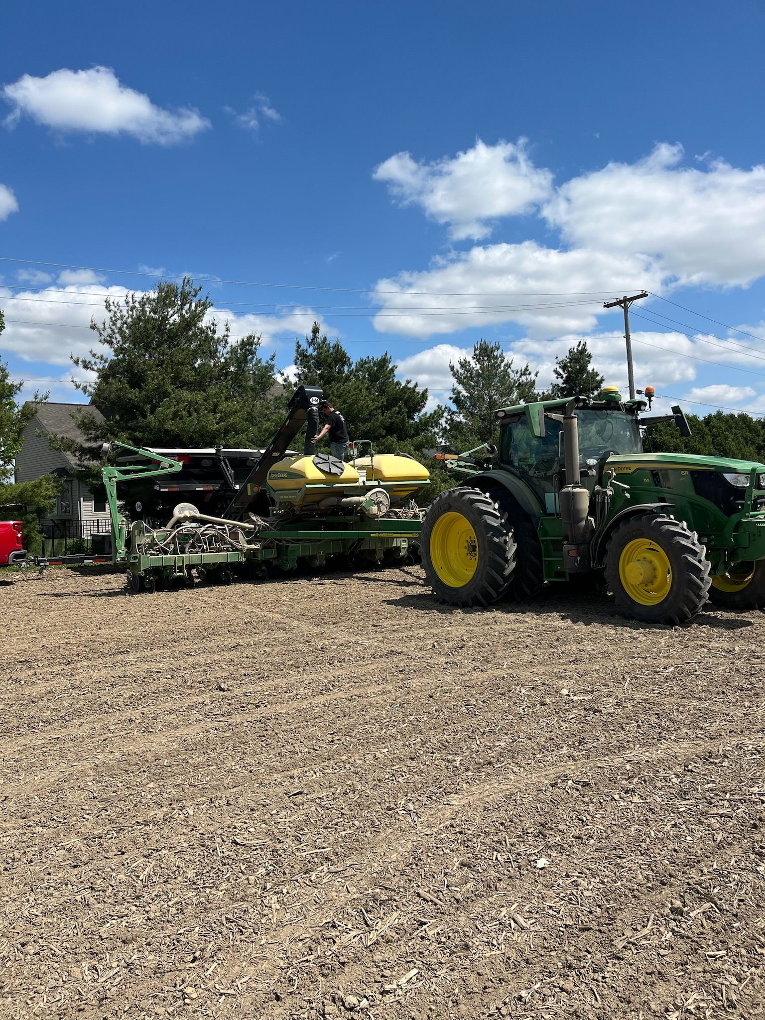 Green John Deere tractor pulling a planter on a gravel lot under a blue sky.