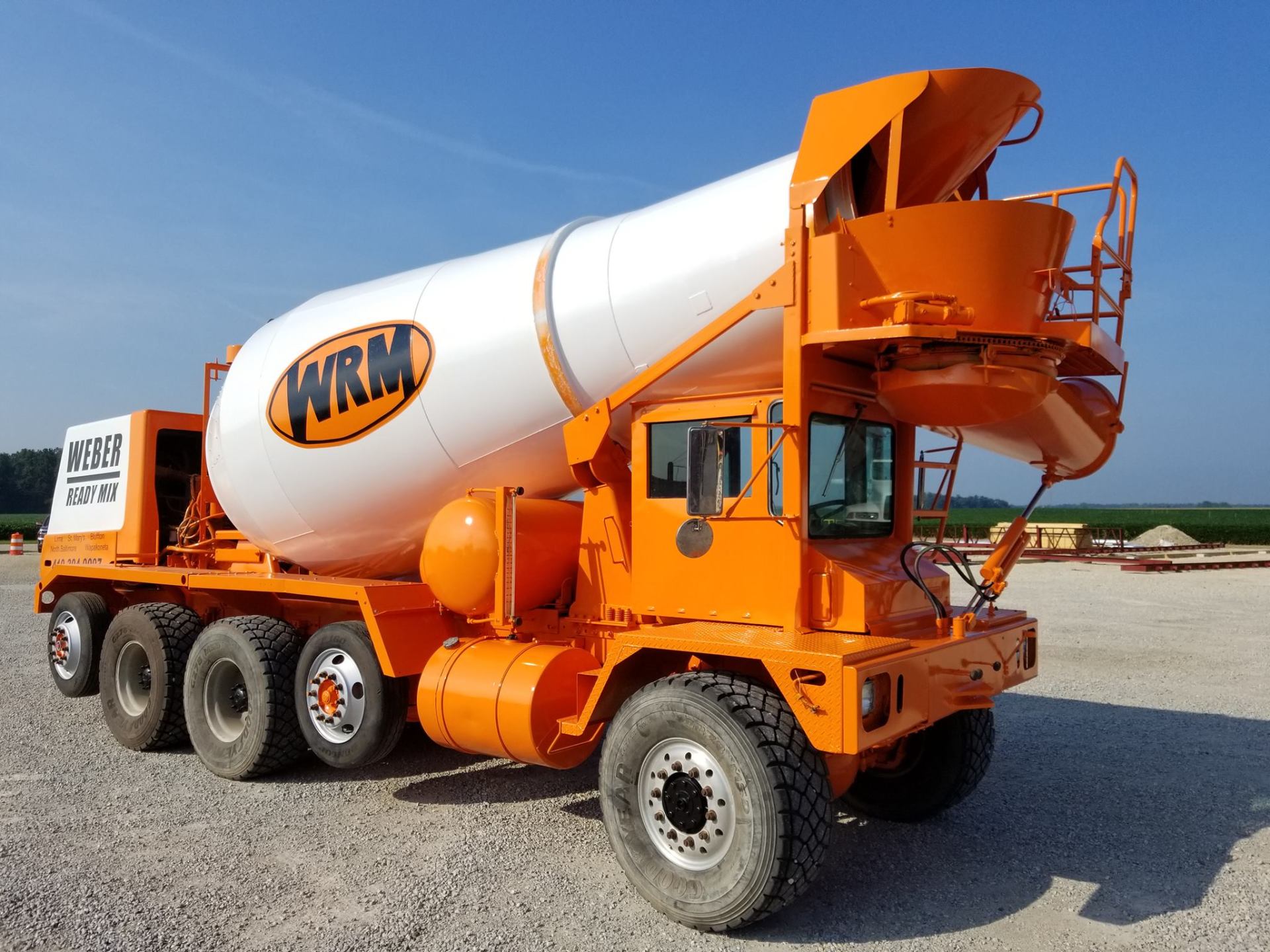 Orange and white concrete mixer truck on a gravel lot.