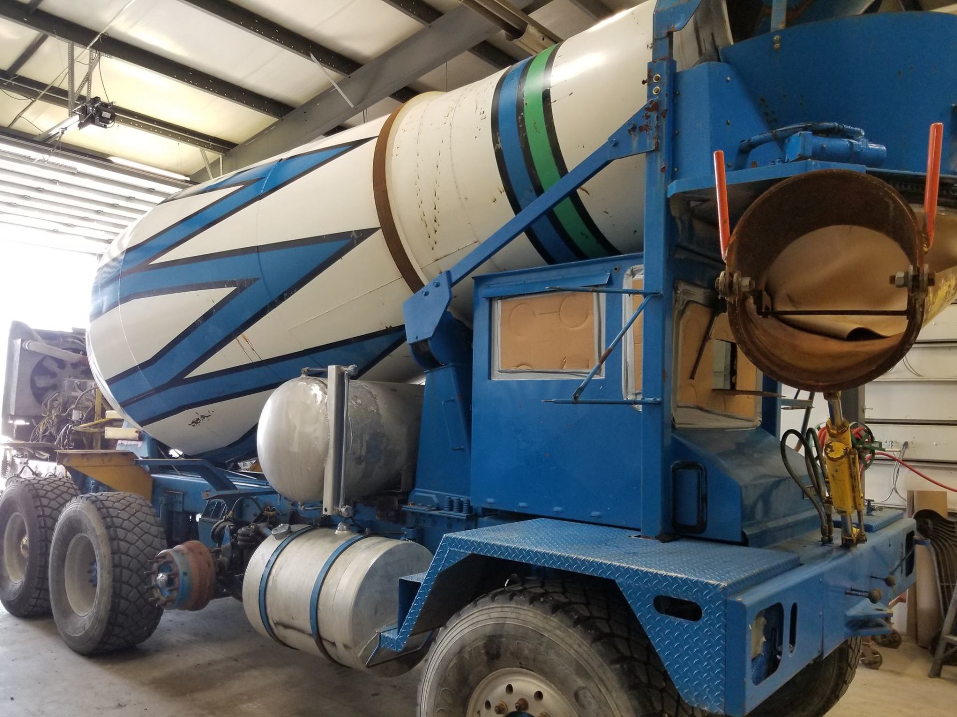 Blue concrete mixer truck with white drum, chevron design, inside a garage.