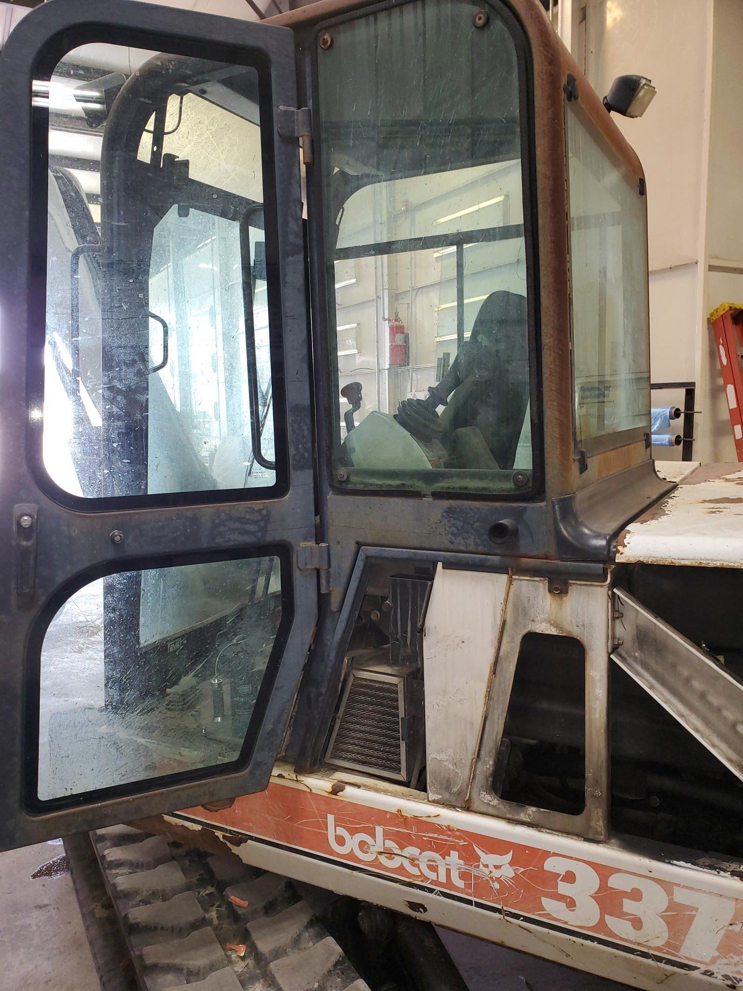 Bobcat 337 compact excavator with open door; interior visible.