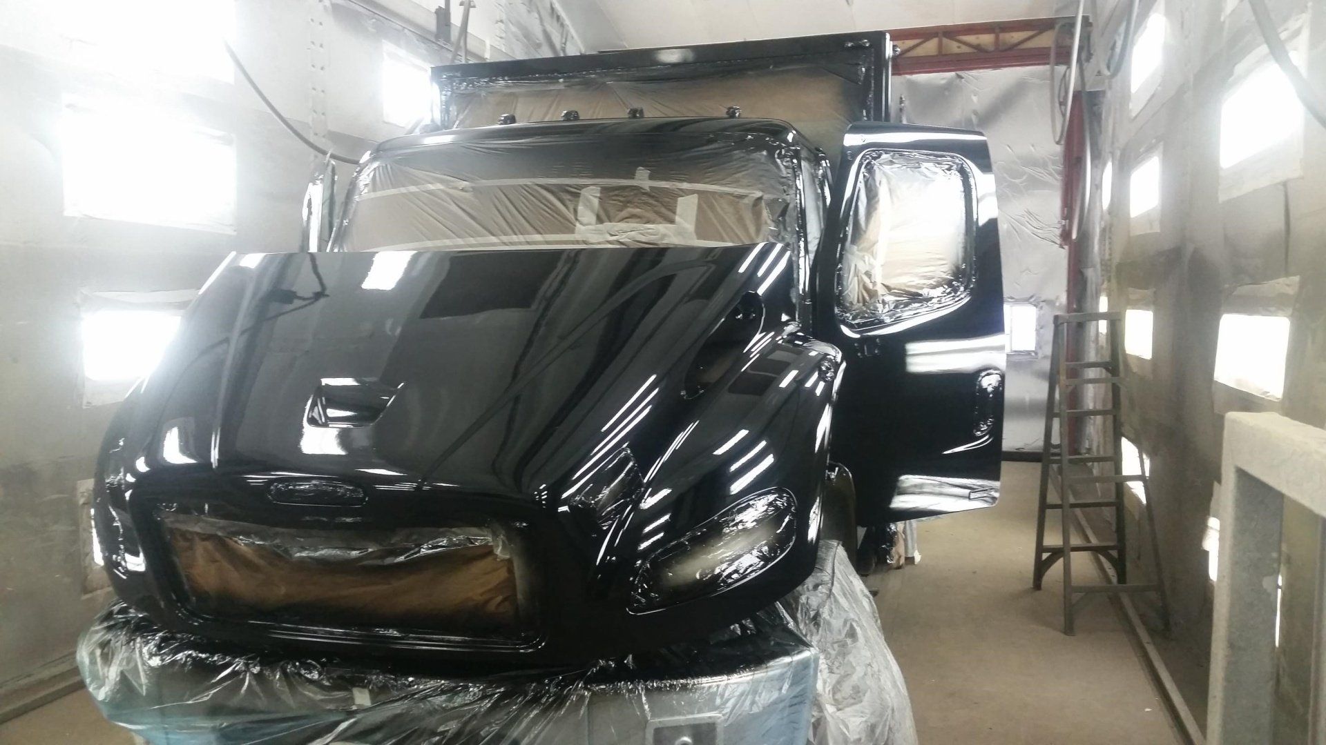 Truck cab being painted black in a spray booth, doors open.