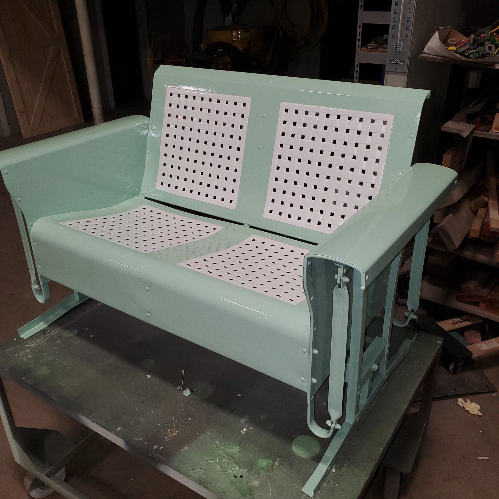 Light green metal glider bench with white perforated seat and backrest.