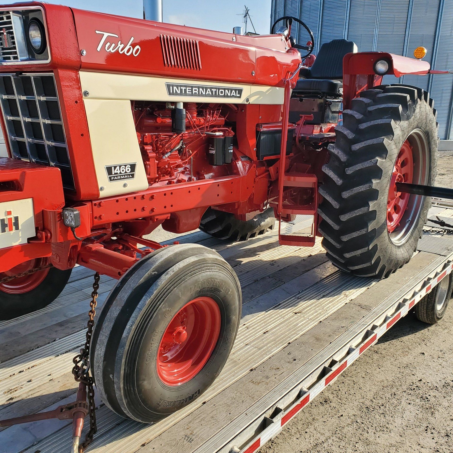 Red and white International Harvester 1466 Turbo tractor parked on a trailer in front of a metal building.