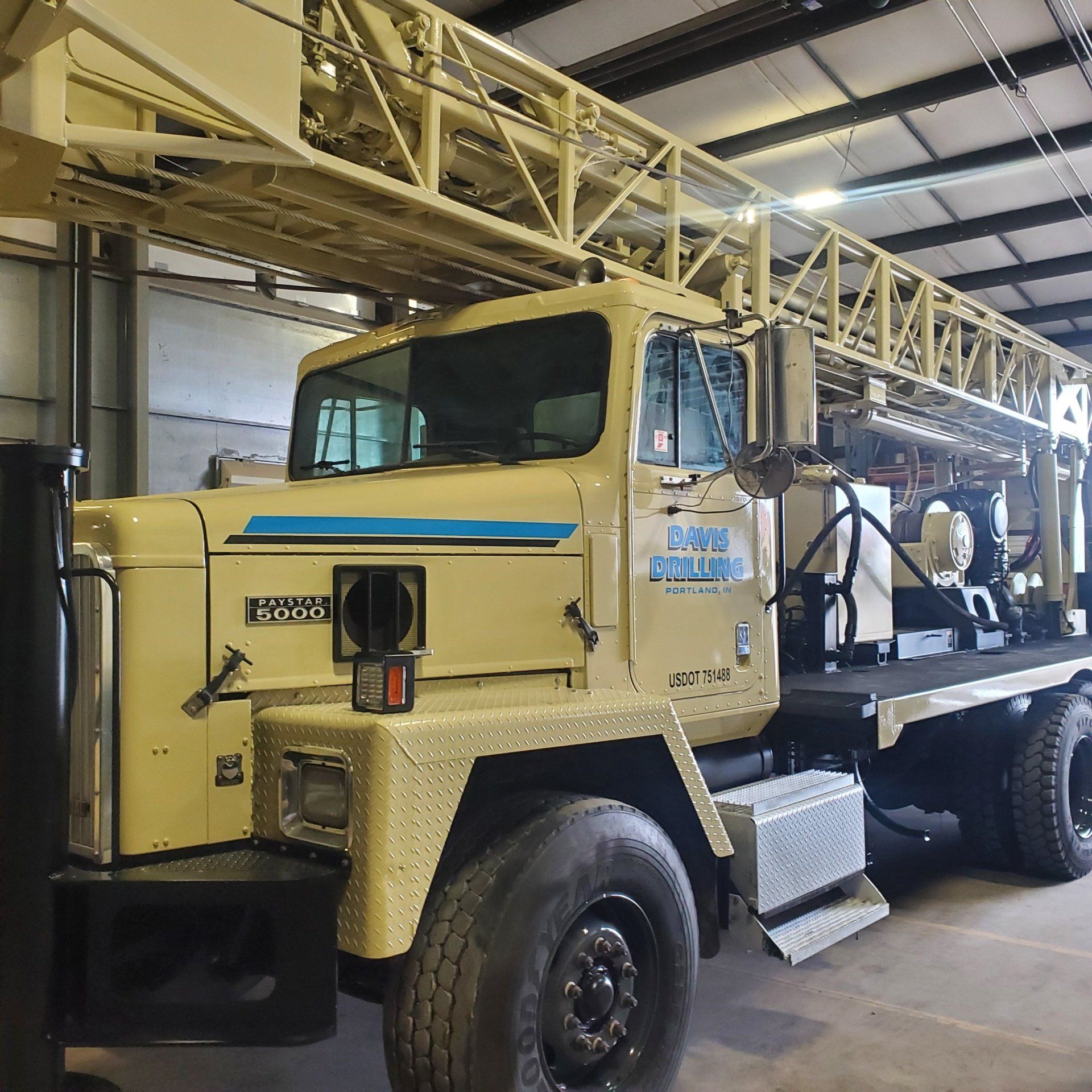 Tan drilling truck parked inside a building, with a drilling rig extending above the cab.